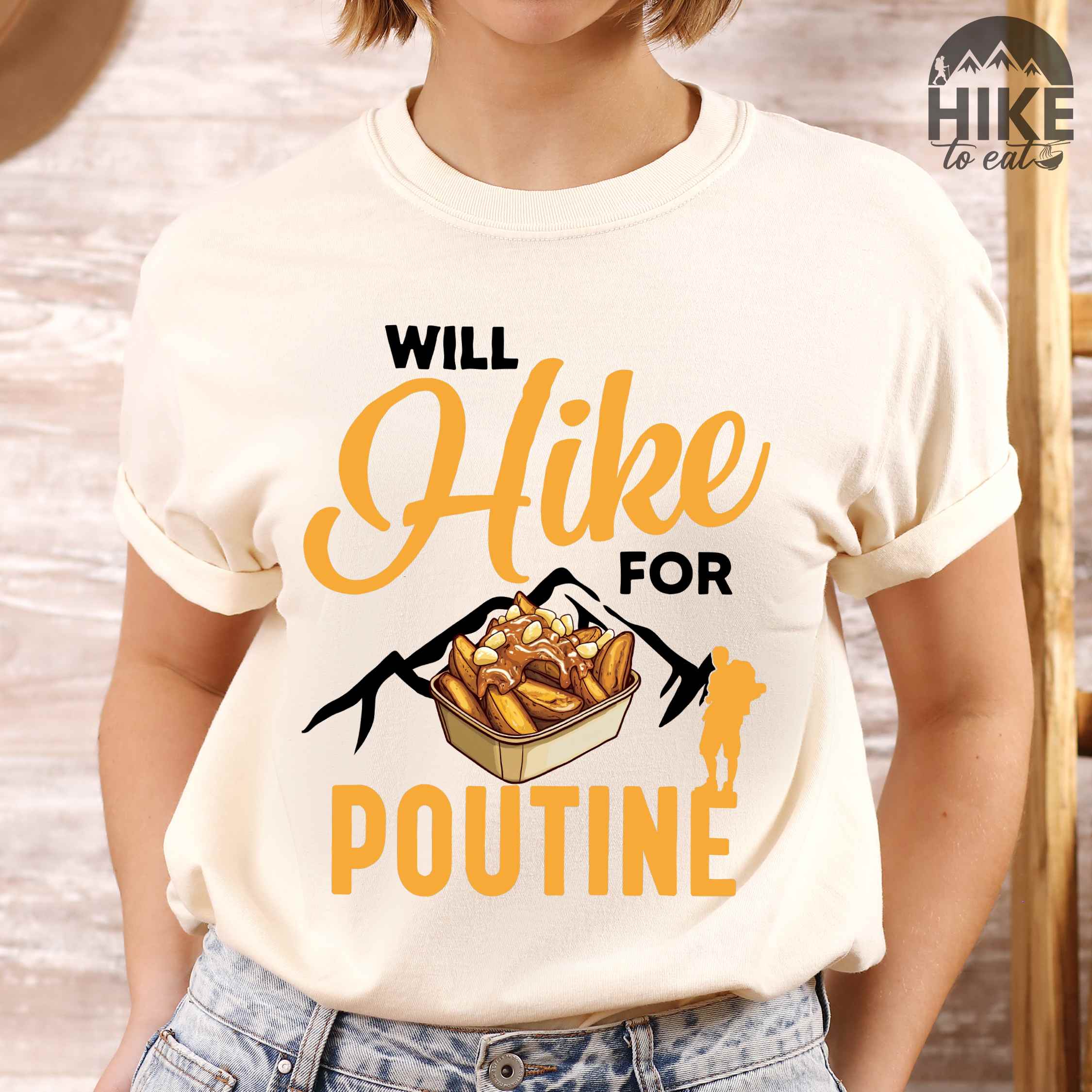 Woman wearing ivory "Will hike for poutine" colored vintage tee with bold typography, mountains, illustrated a serving of poutine and backpackers looking for comfort food.