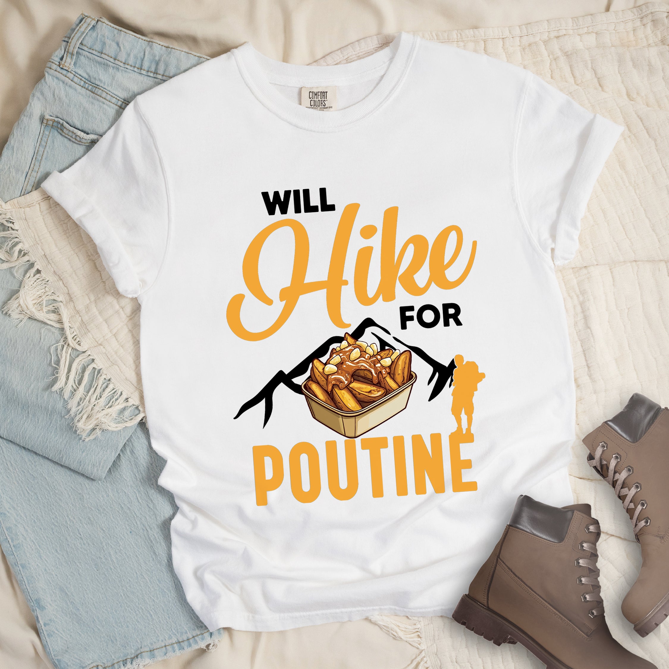 White t-shirt with orange and black text reading "WILL Hike FOR POUTINE". "WILL" appears in black at the top, "Hike" in large orange script in the middle, "FOR" in black, and "POUTINE" in large orange letters at the bottom. Features a detailed illustration of a container of poutine (french fries with cheese curds and gravy) in the center, black mountain silhouettes behind it, and an orange hiker silhouette on the right.