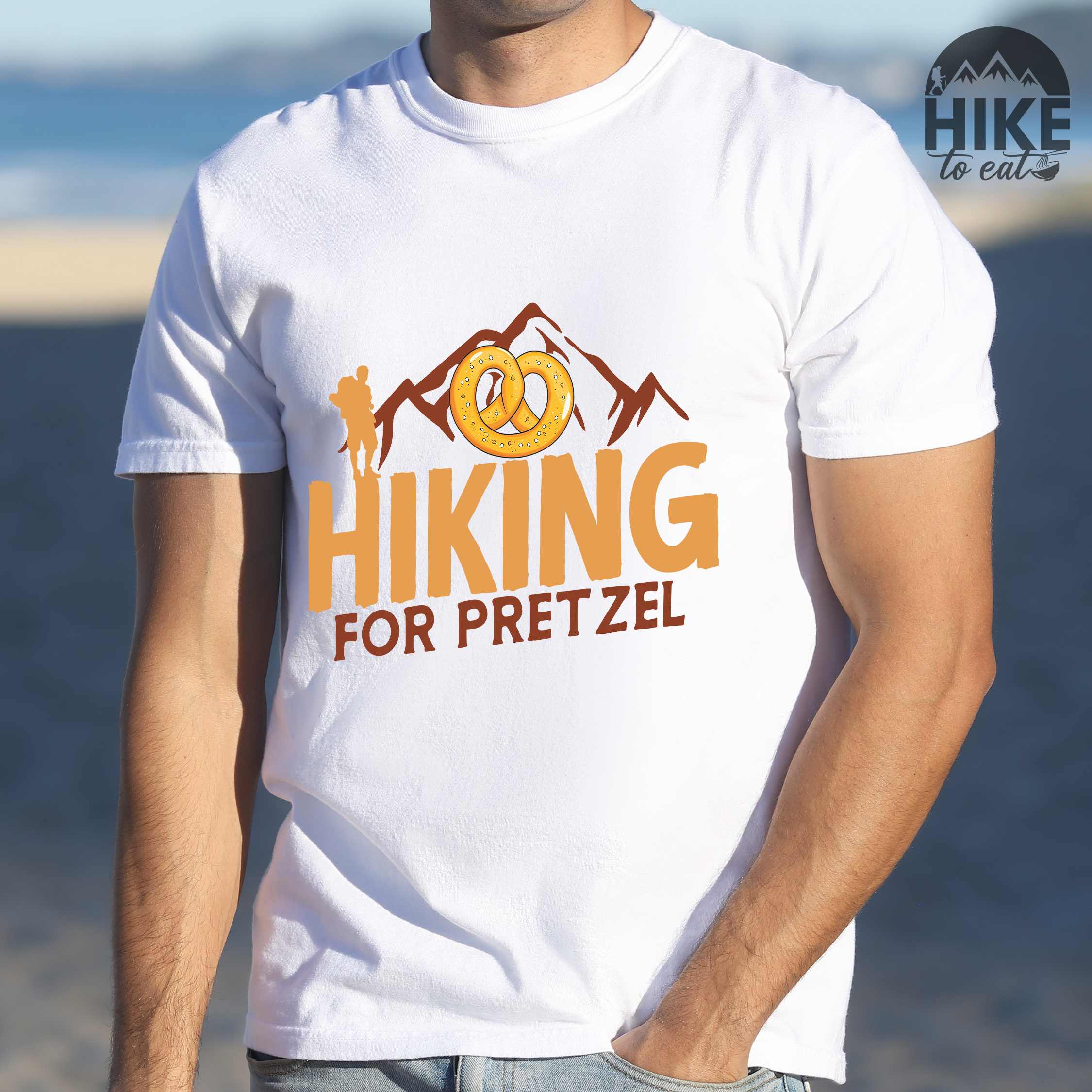 Man wearing white "Hiking for pretzel" colored vintage tee with bold typography, mountains, birds, and illustrated pretzel for baked pretzel lovers
