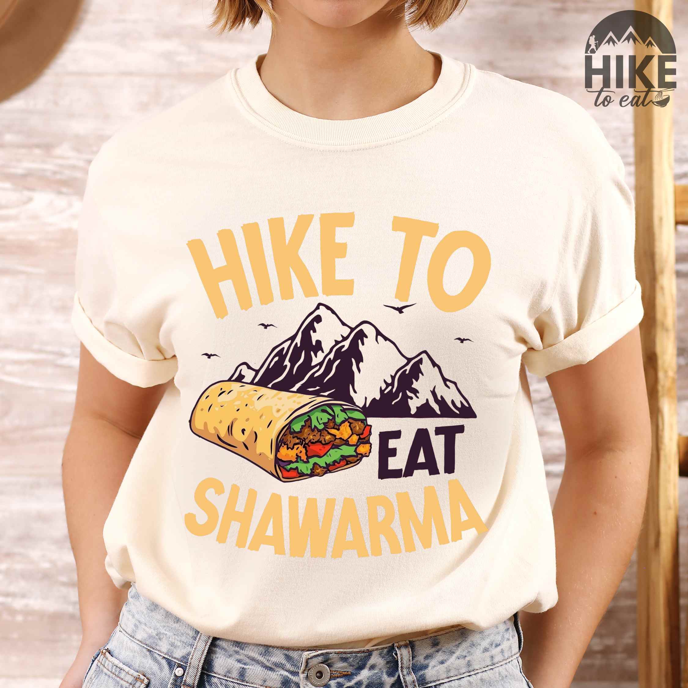 Woman wearing ivory "Hike to Eat Shawarma" colored vintage tee with bold typography, mountains, birds, and illustrated shawarma, and backpackers for shawarma lovers.