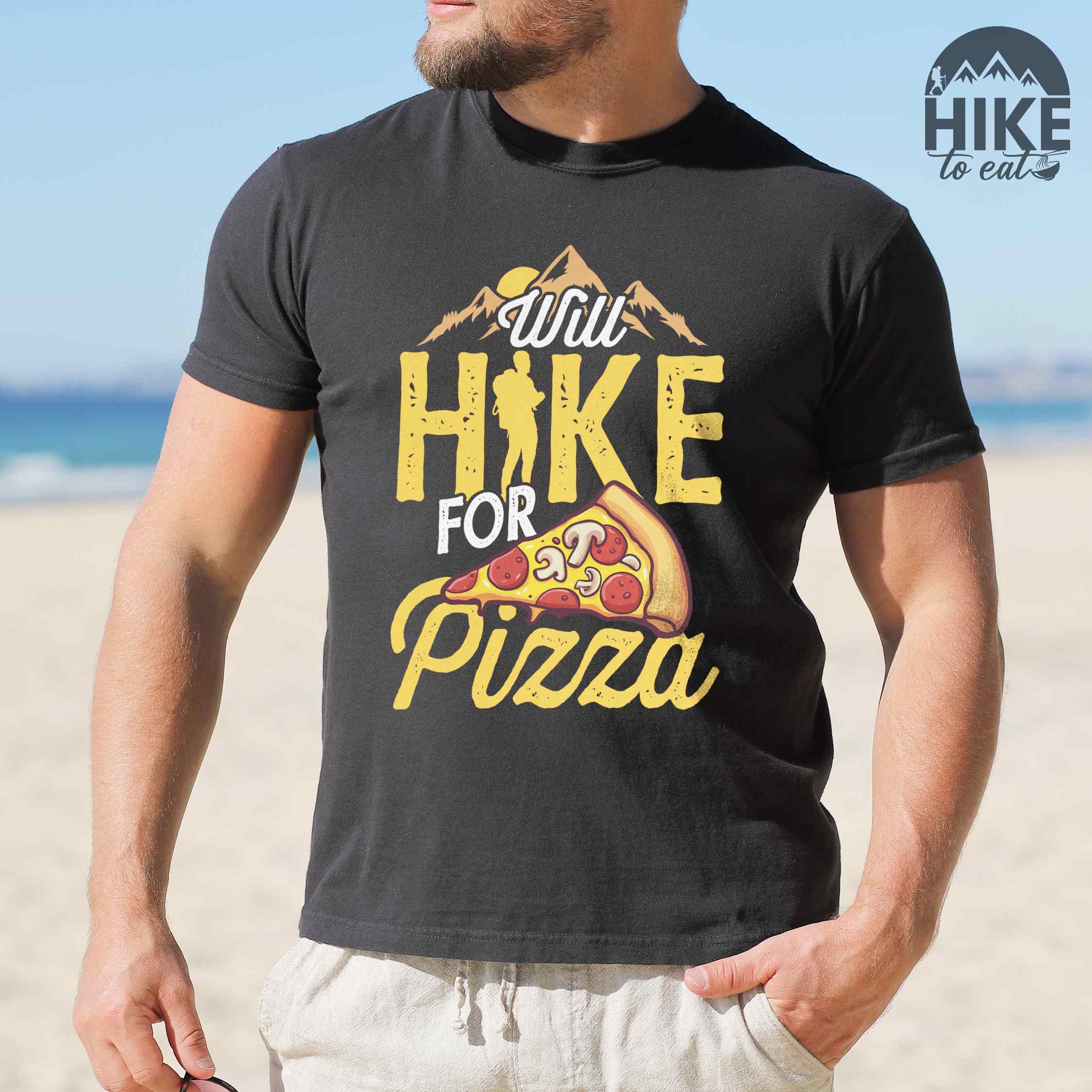 Man wearing black colored vintage tee featuring Hiking design of mountains with a sunrise behind and a slice of pizza in front of the phrase 'Will Hike for Pizza'.