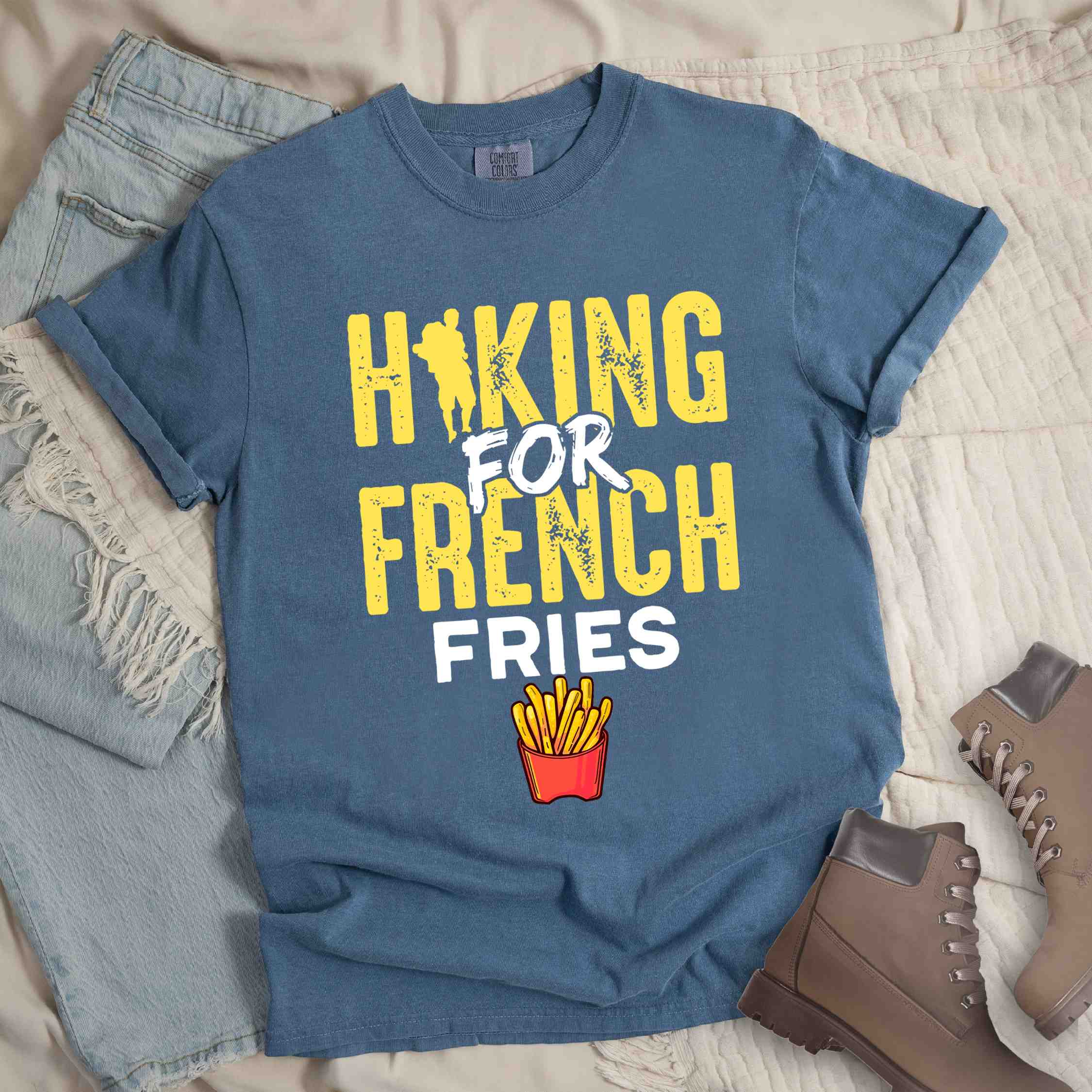 Blue jean "Hiking for french fries" colored vintage tee with bold typography, mountains, illustrated fries, and backpacker for comfort food enthusiasts.