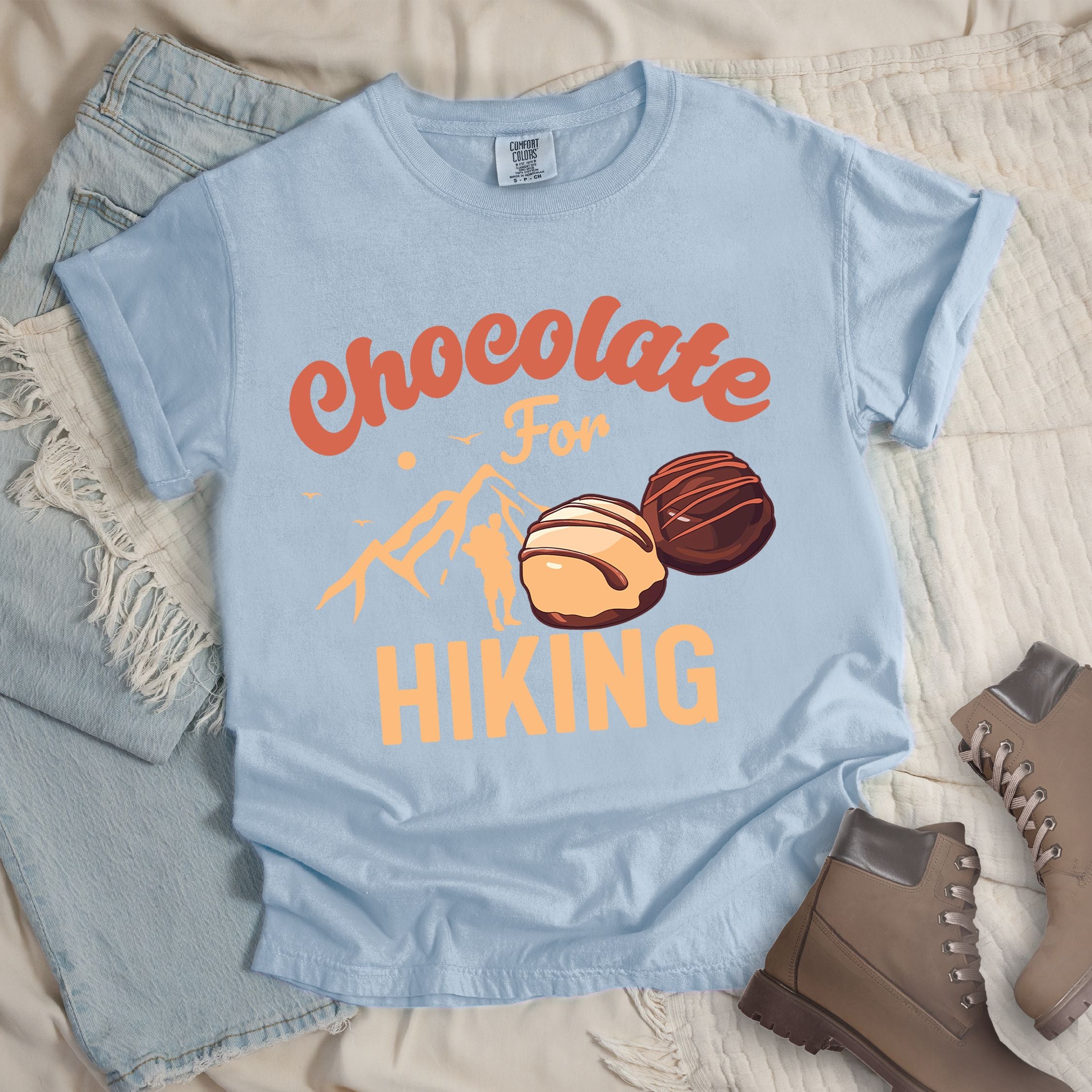 Light blue shirt with the phrase “Chocolate For Hiking.” Features a mountain outline, hiker silhouette, and two chocolate truffles illustration.