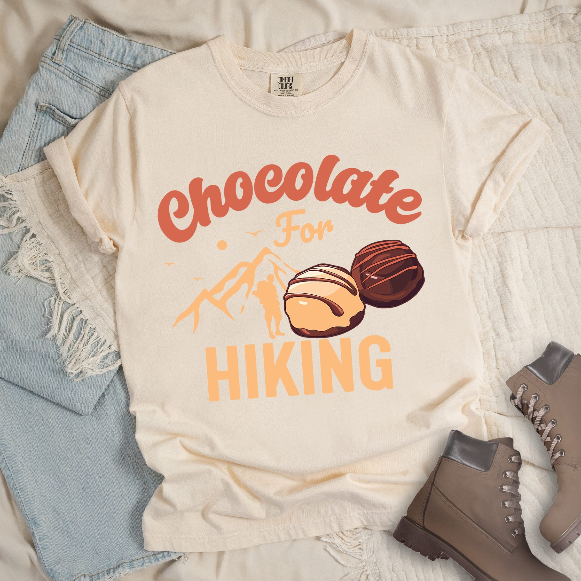 Ivory shirt with the phrase “Chocolate For Hiking.” Features a mountain outline, hiker silhouette, and two chocolate truffles illustration.