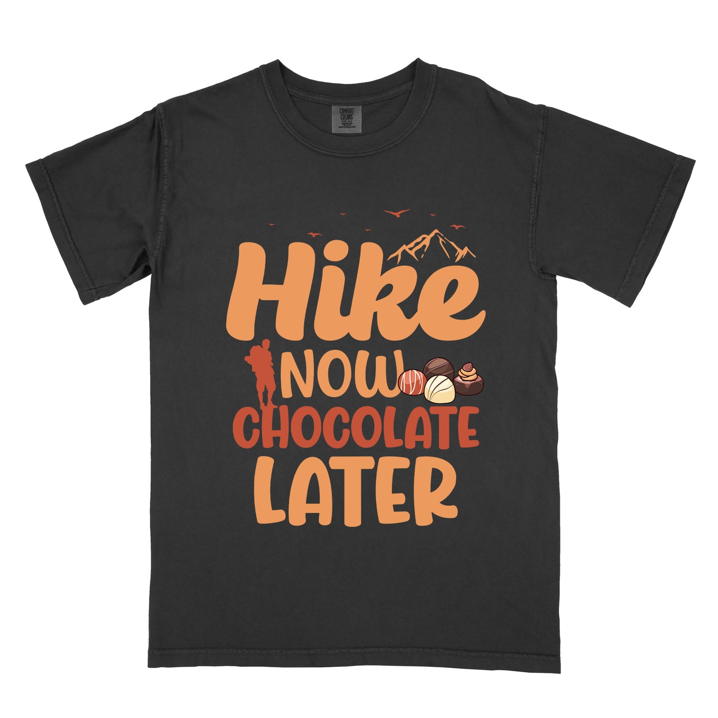 Black t-shirt with orange and brown text reading "Hike NOW CHOCOLATE LATER". "Hike" appears in large orange at the top with small orange mountain silhouettes and bird silhouettes, "NOW" in lighter orange with a red hiker silhouette, "CHOCOLATE" in brown, and "LATER" in orange at the bottom. Features illustrations of various chocolate truffles between "NOW" and "CHOCOLATE".
