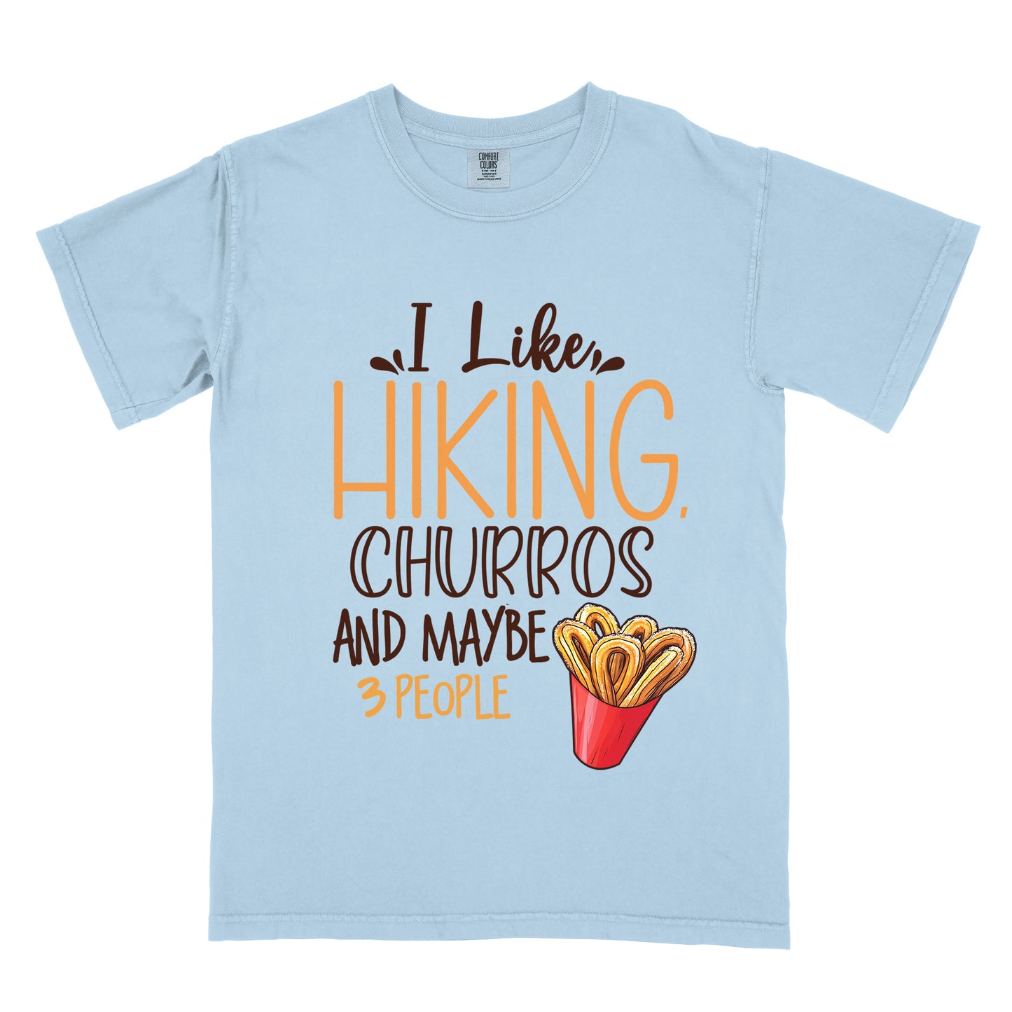 Chambray (Light Blue) t-shirt with deep brown and orange text reading "I Like HIKING, CHURROS AND MAYBE 3 PEOPLE". "I Like" appears in deep brown script at the top, "HIKING," in large orange letters, "CHURROS" in deep brown outlined letters, "AND MAYBE" in deep brown, and "3 PEOPLE" in small orange text at the bottom. Features an illustration of churros in a red container on the right side.