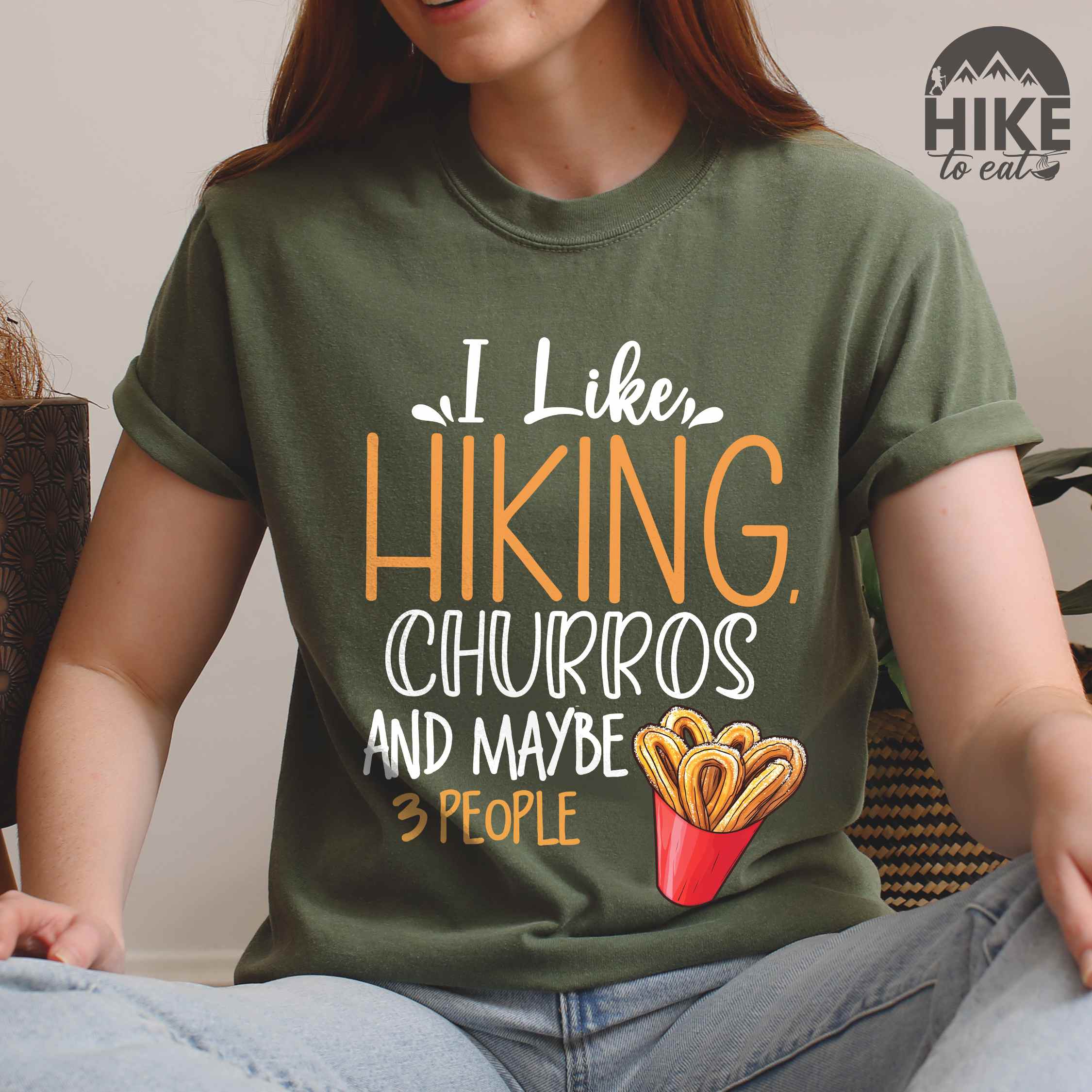 woman wearing moss "I like hiking, churros and maybe three people " colored vintage tee with bold typography, mountains, illustrated a serving of Churros, and backpackers with a sweet tooth.