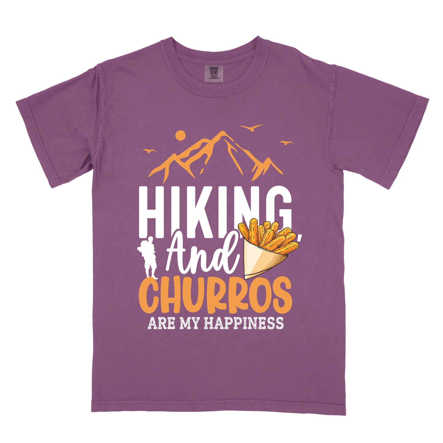 Berry (Dark Violet) t-shirt with orange and white text reading "HIKING And CHURROS ARE MY HAPPINESS". "HIKING" appears in large white letters, "And" in white script, "CHURROS" in orange, and "ARE MY HAPPINESS" in small white text at the bottom. Features orange mountain silhouettes with sun and birds at the top, a white hiker silhouette, and an illustration of churros in a paper cone.