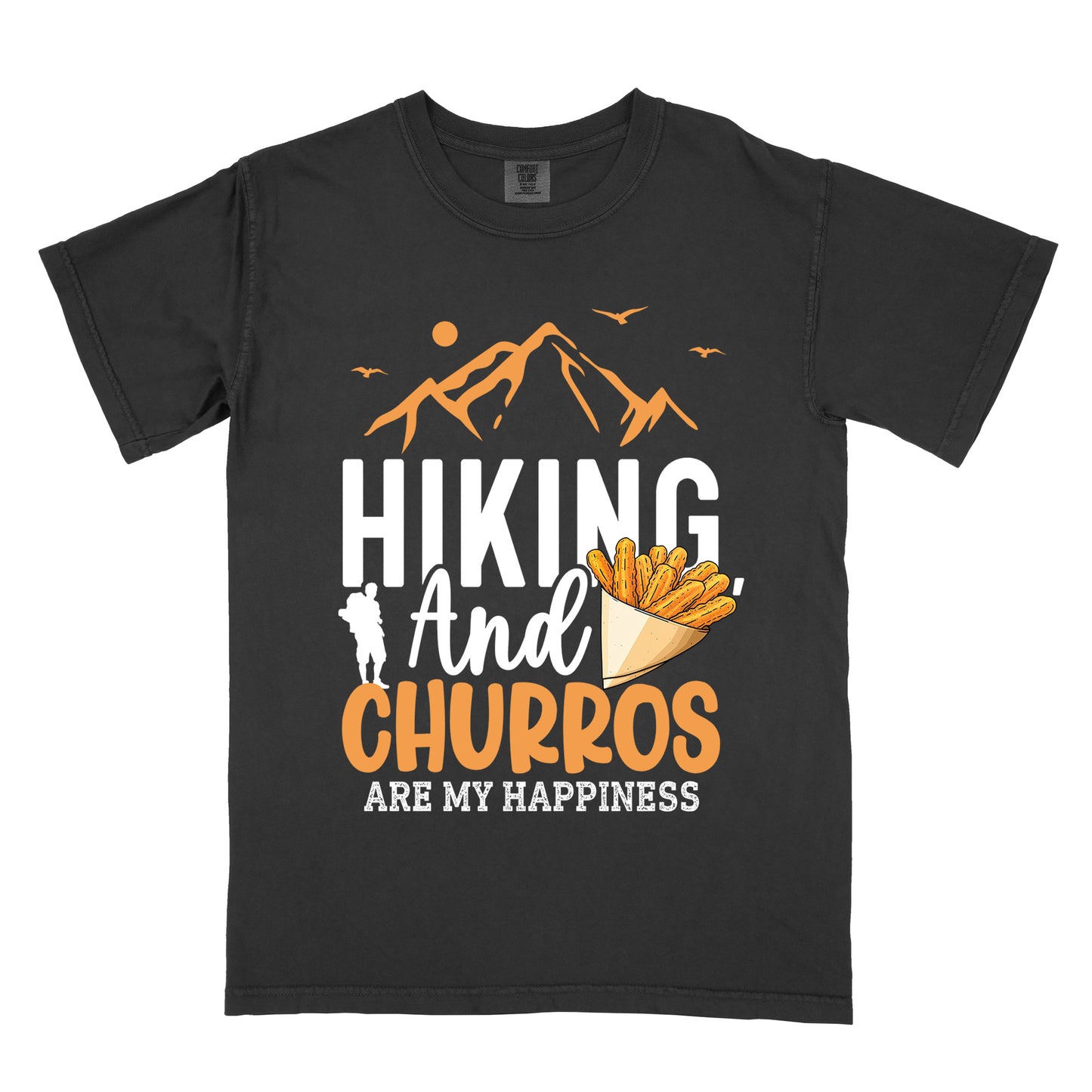 Black t-shirt with orange and white text reading "HIKING And CHURROS ARE MY HAPPINESS". "HIKING" appears in large white letters, "And" in white script, "CHURROS" in orange, and "ARE MY HAPPINESS" in small white text at the bottom. Features orange mountain silhouettes with sun and birds at the top, a white hiker silhouette, and an illustration of churros in a paper cone.