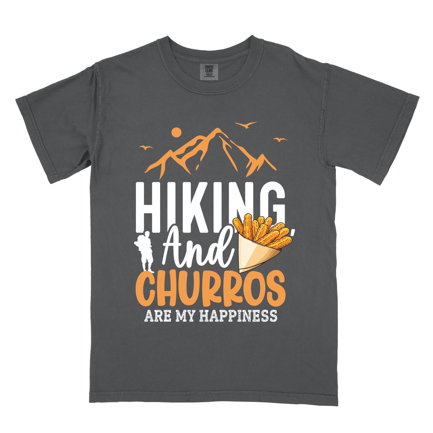 Graphite (Deep Gray) t-shirt with orange and white text reading "HIKING And CHURROS ARE MY HAPPINESS". "HIKING" appears in large white letters, "And" in white script, "CHURROS" in orange, and "ARE MY HAPPINESS" in small white text at the bottom. Features orange mountain silhouettes with sun and birds at the top, a white hiker silhouette, and an illustration of churros in a paper cone.
