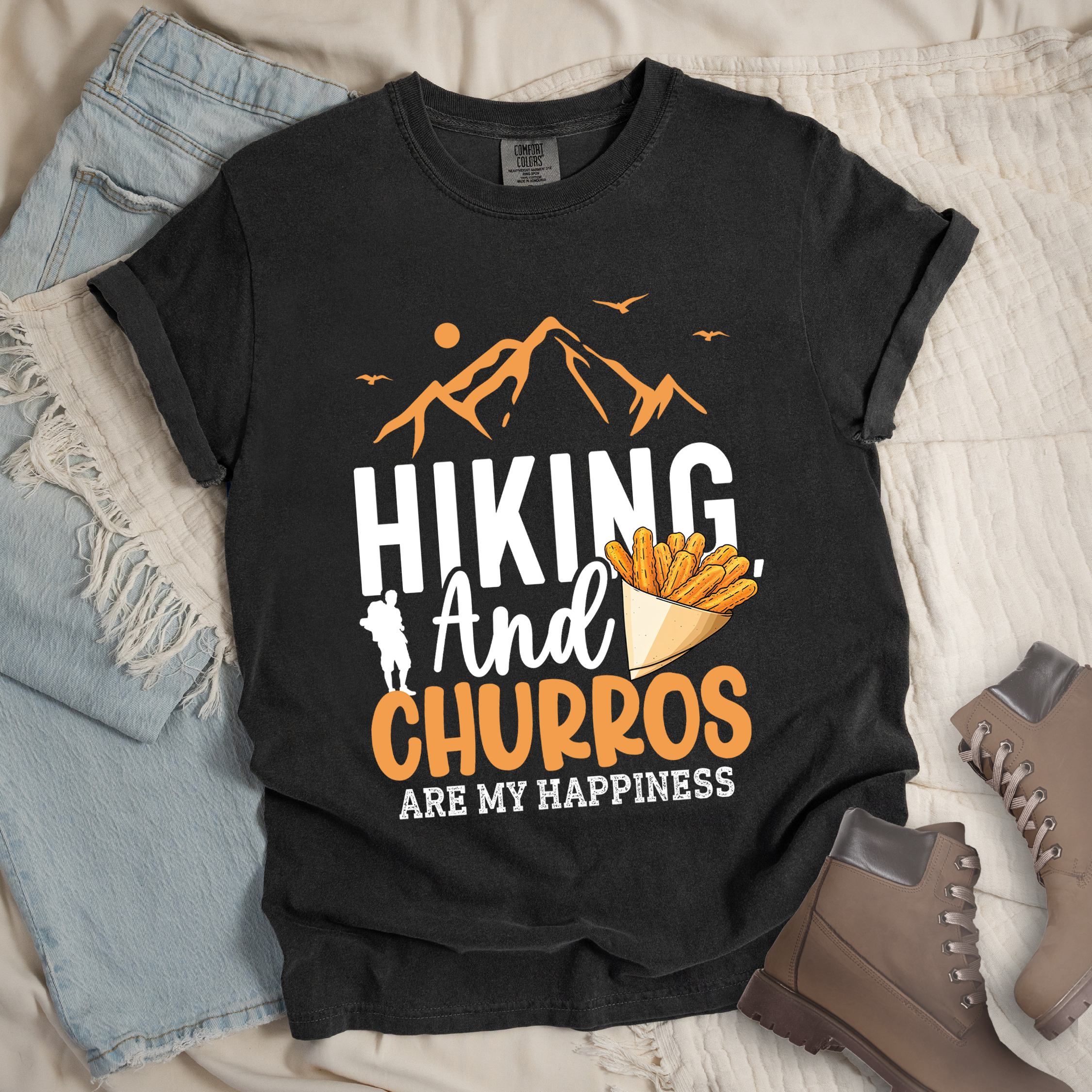 Dark grey shirt with the phrase “Hiking And Churros Are My Happiness.” Features a hiker silhouette, mountains, birds, and a churros cone illustration.