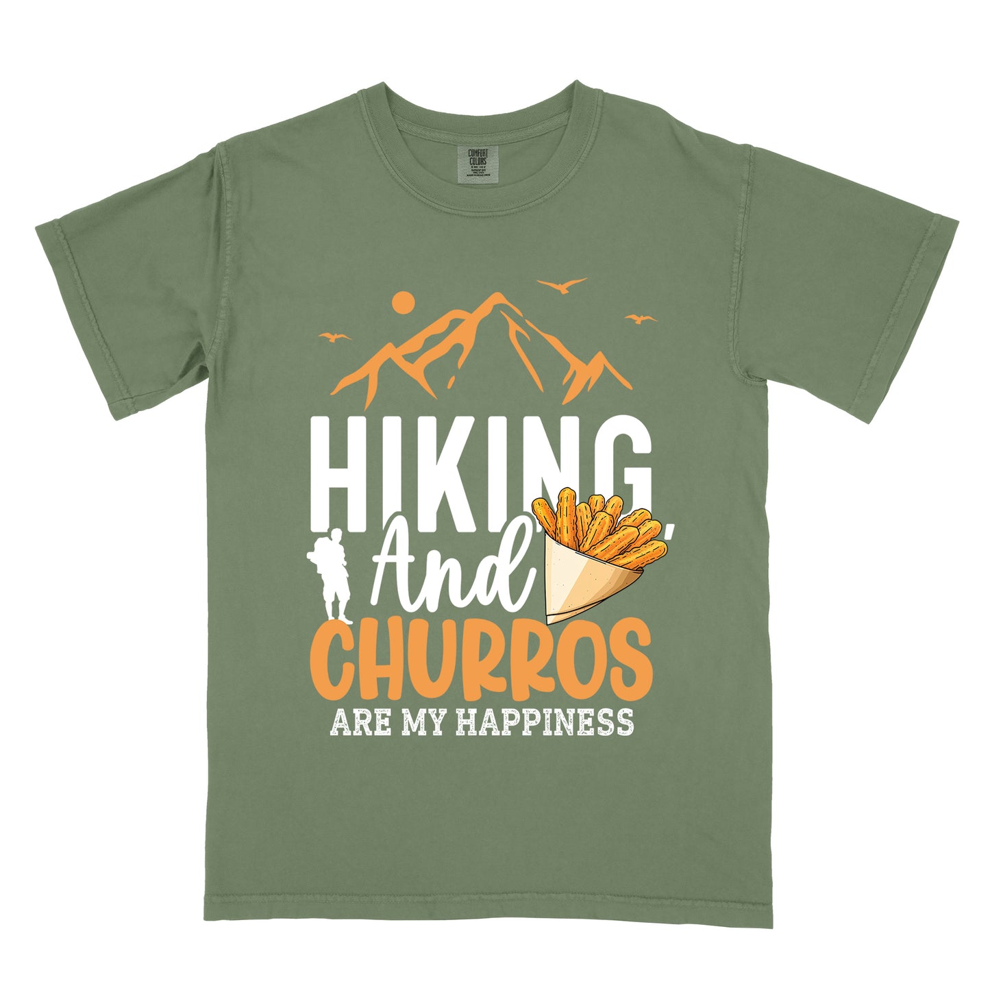 Moss (Dark Green) t-shirt with orange and white text reading "HIKING And CHURROS ARE MY HAPPINESS". "HIKING" appears in large white letters, "And" in white script, "CHURROS" in orange, and "ARE MY HAPPINESS" in small white text at the bottom. Features orange mountain silhouettes with sun and birds at the top, a white hiker silhouette, and an illustration of churros in a paper cone.