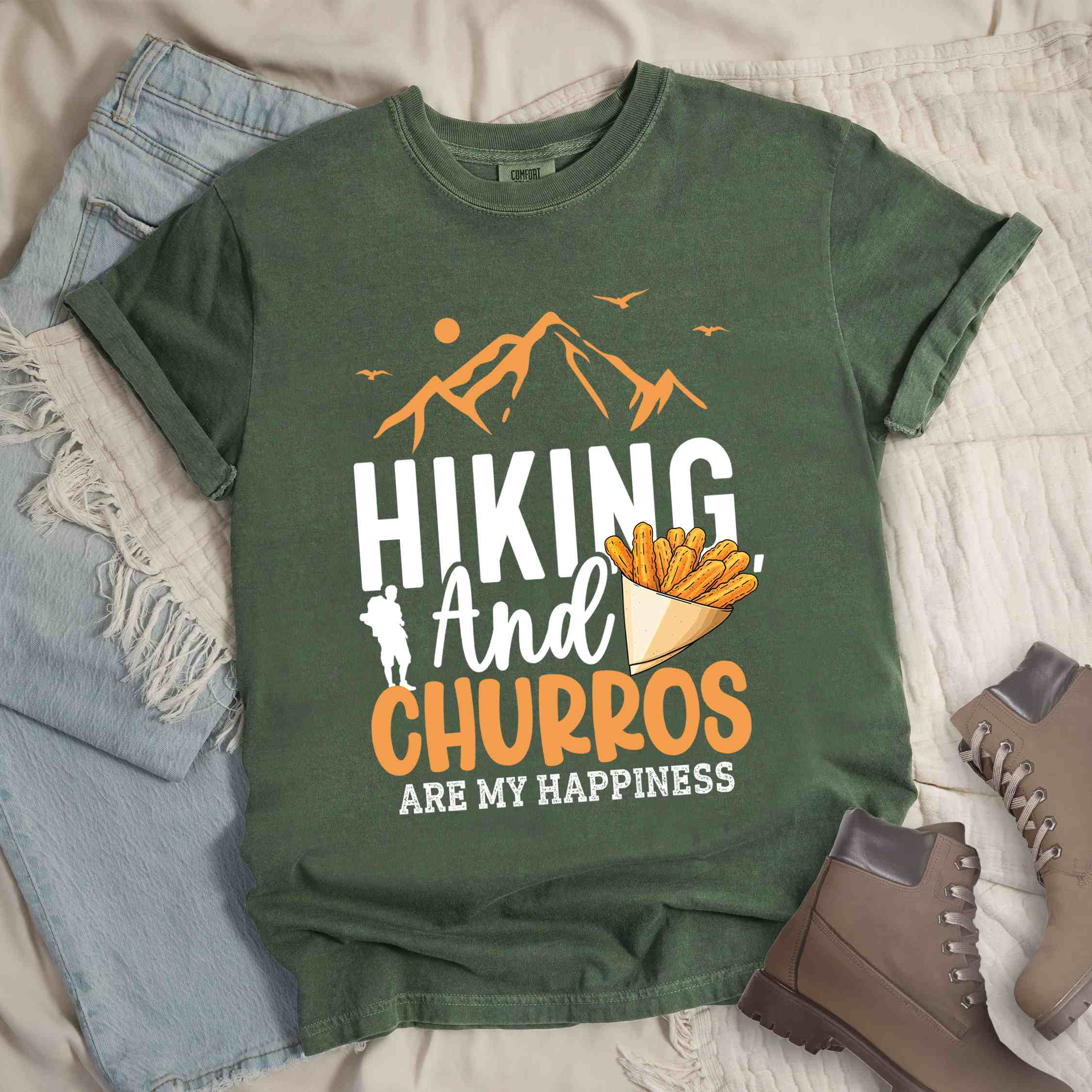Moss "hiking and churros are my happiness " colored vintage tee with bold typography, mountains, birds, illustrated a serving of Churros, and backpackers with a sweet tooth.