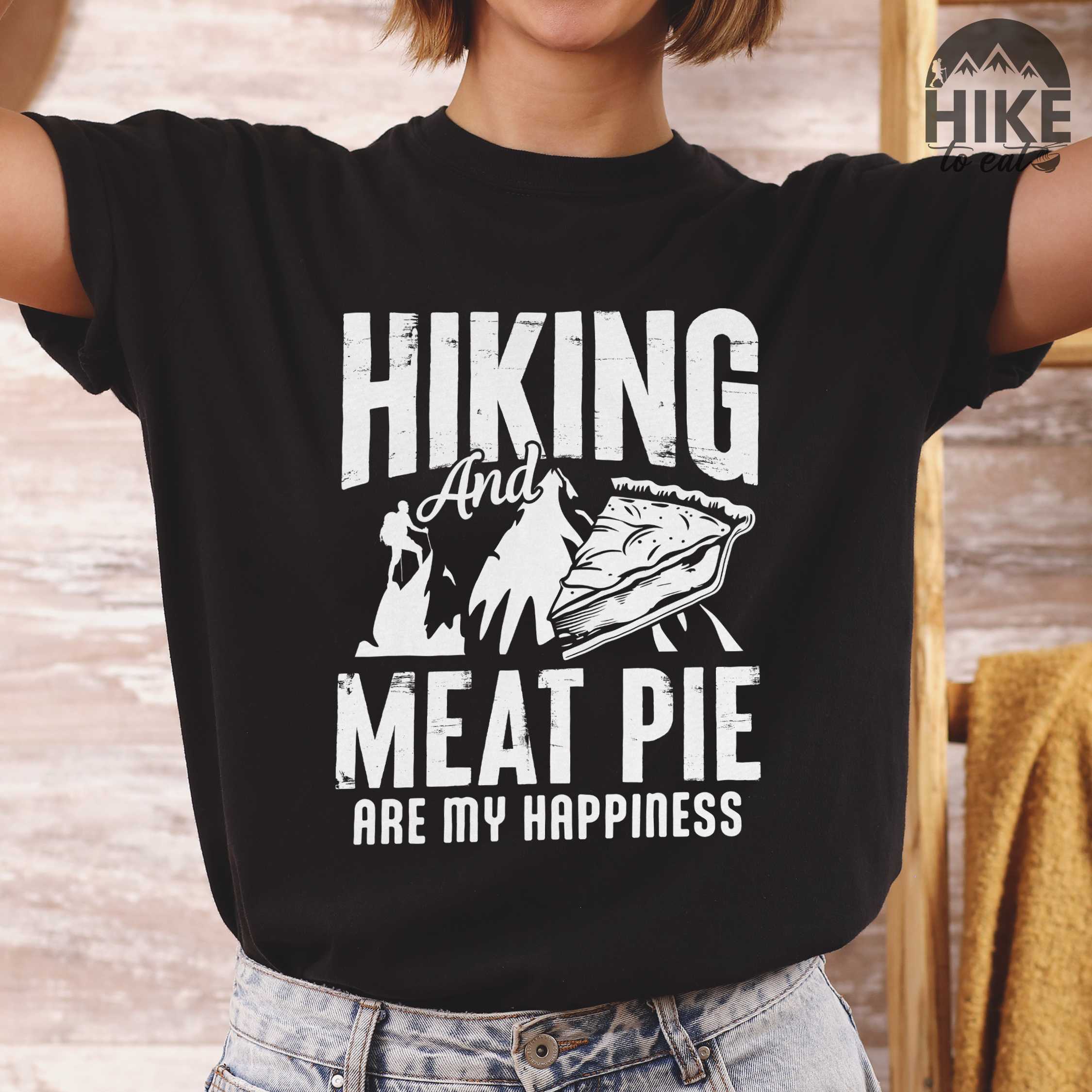 Woman wearing black "Hiking and Meat Pie are my Happiness" colored vintage tee with bold typography, mountains, and illustrated slice of pie for pie lovers