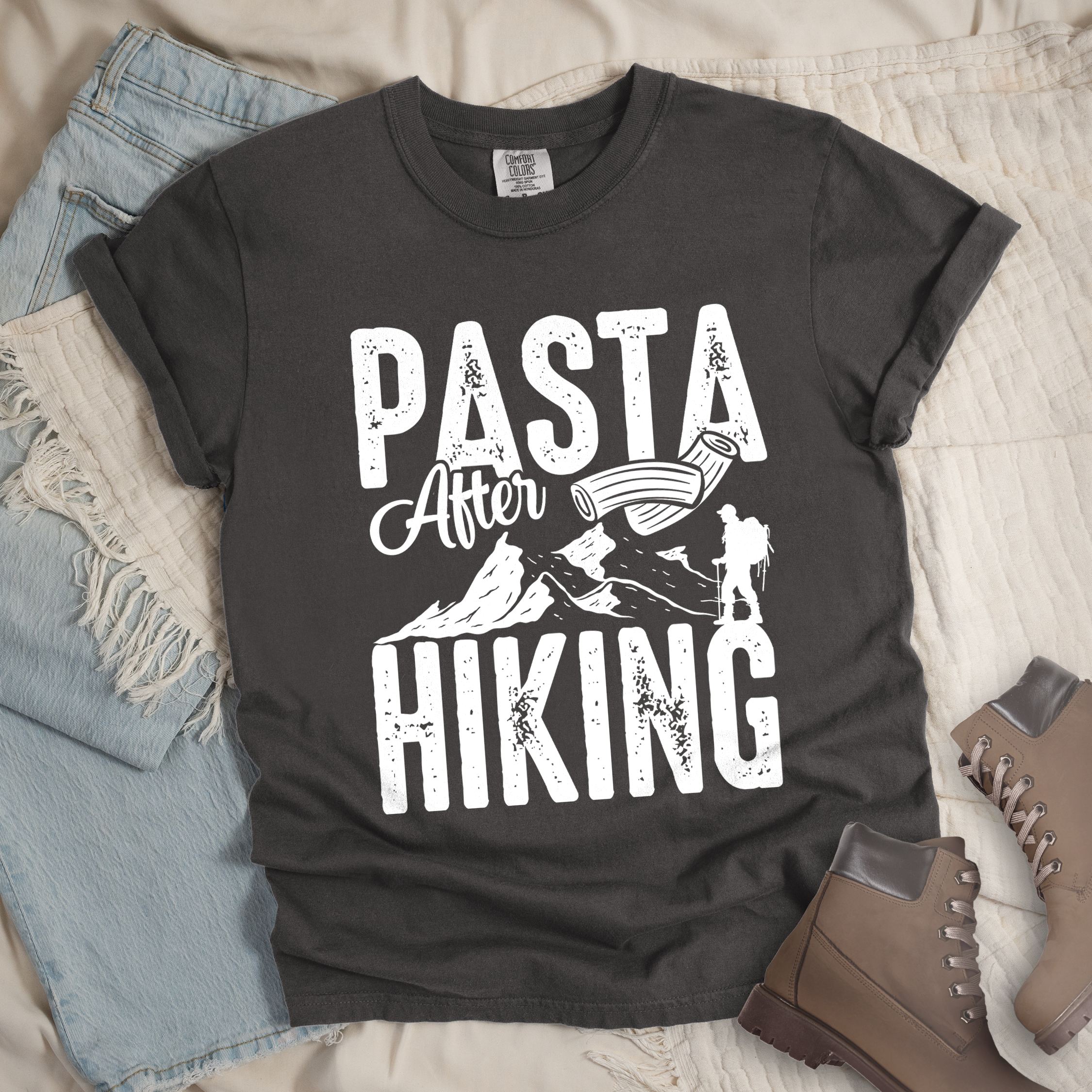 Dark grey shirt with the phrase “Pasta After Hiking.” Includes a hiker silhouette, mountain outline, and pasta noodle illustration.