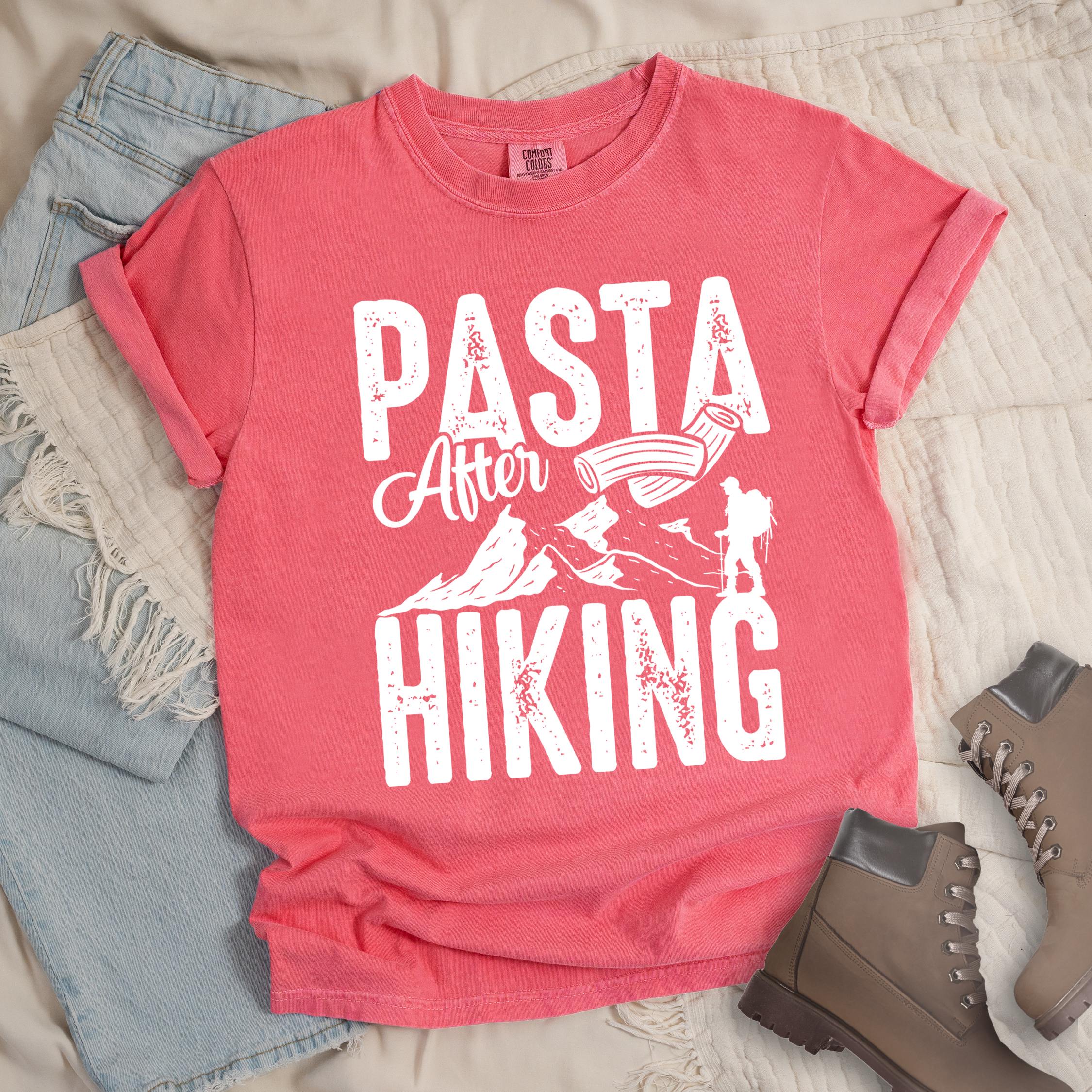 Pink shirt with the phrase “Pasta After Hiking.” Includes a hiker silhouette, mountain outline, and pasta noodle illustration.