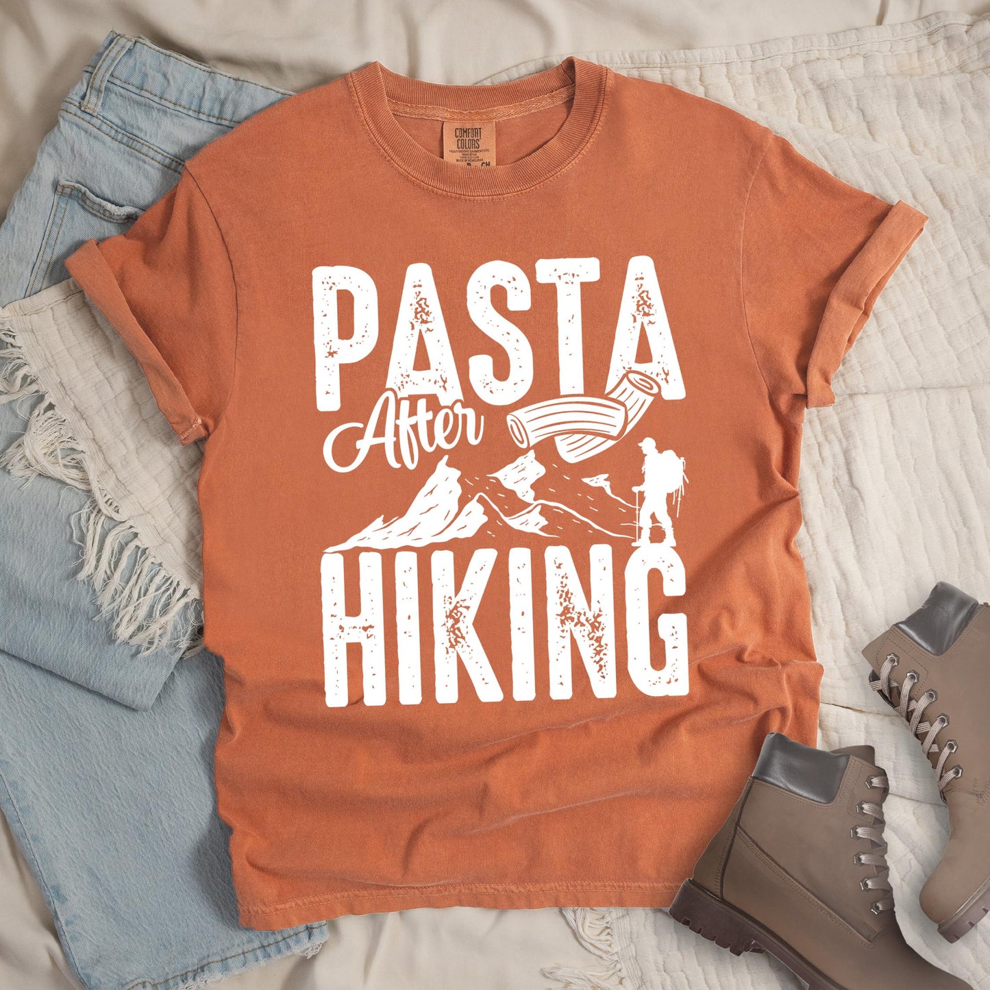 Orange shirt with the phrase “Pasta After Hiking.” Includes a hiker silhouette, mountain outline, and pasta noodle illustration.