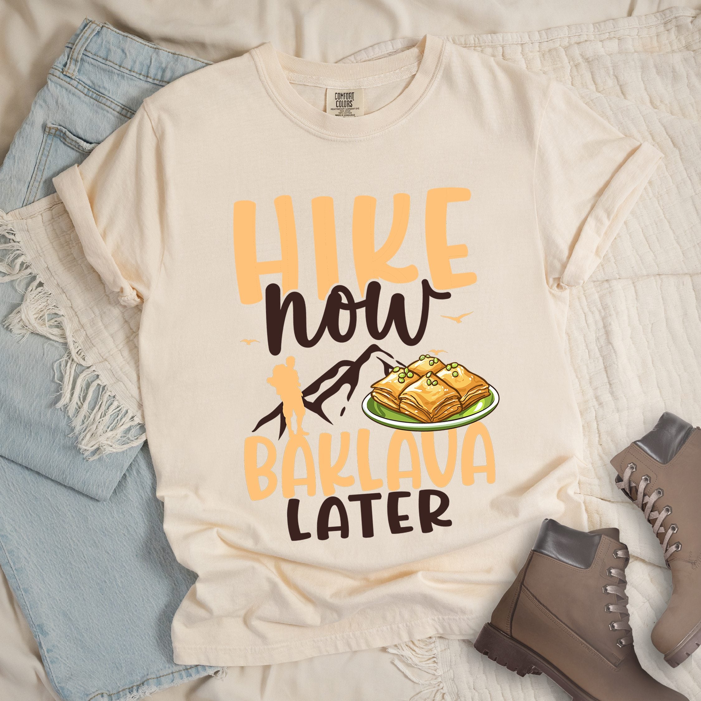 Ivory shirt with Hiking Design featuring the phrase “Will Hike for Baklava” in bold lettering and a colorful illustration of golden baklava on a plate.