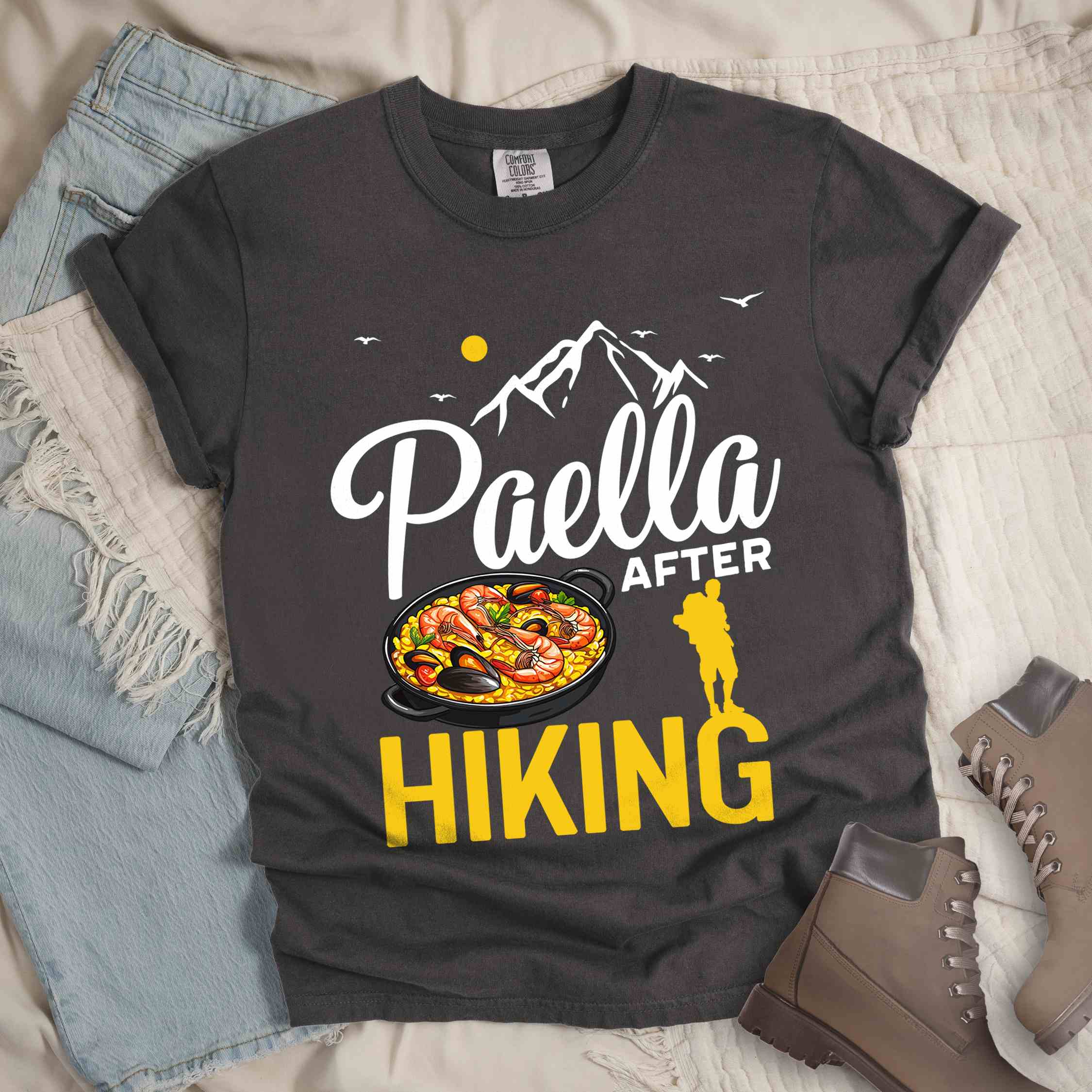 Pepper "Paella after hiking" colored vintage tee with bold typography, mountains, birds, illustrated paella platter, and backpackers for rice lovers.