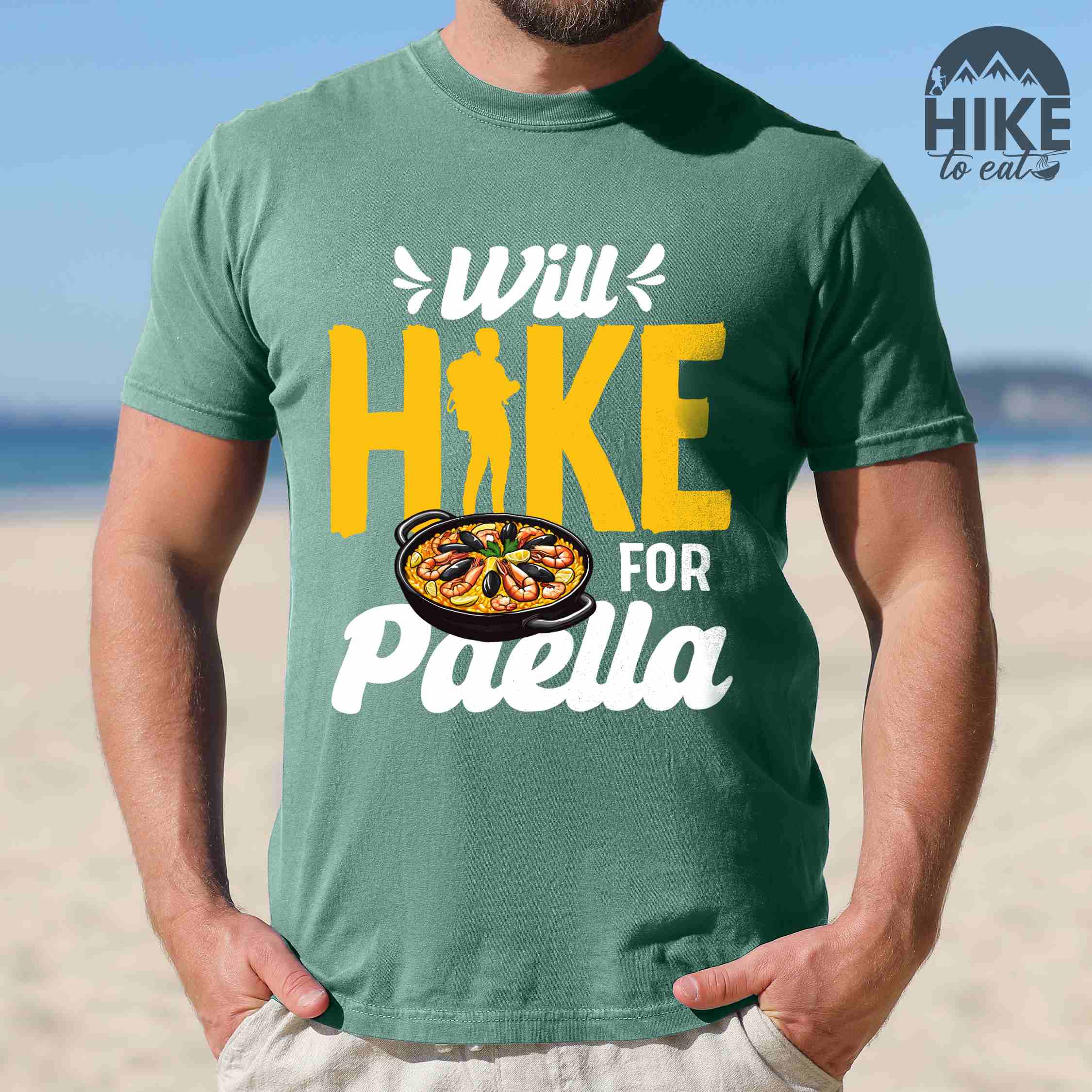 Man wearing light green "Will Hike for Paella" colored vintage tee with bold typography, illustrated paella platter, and backpackers for rice lovers.