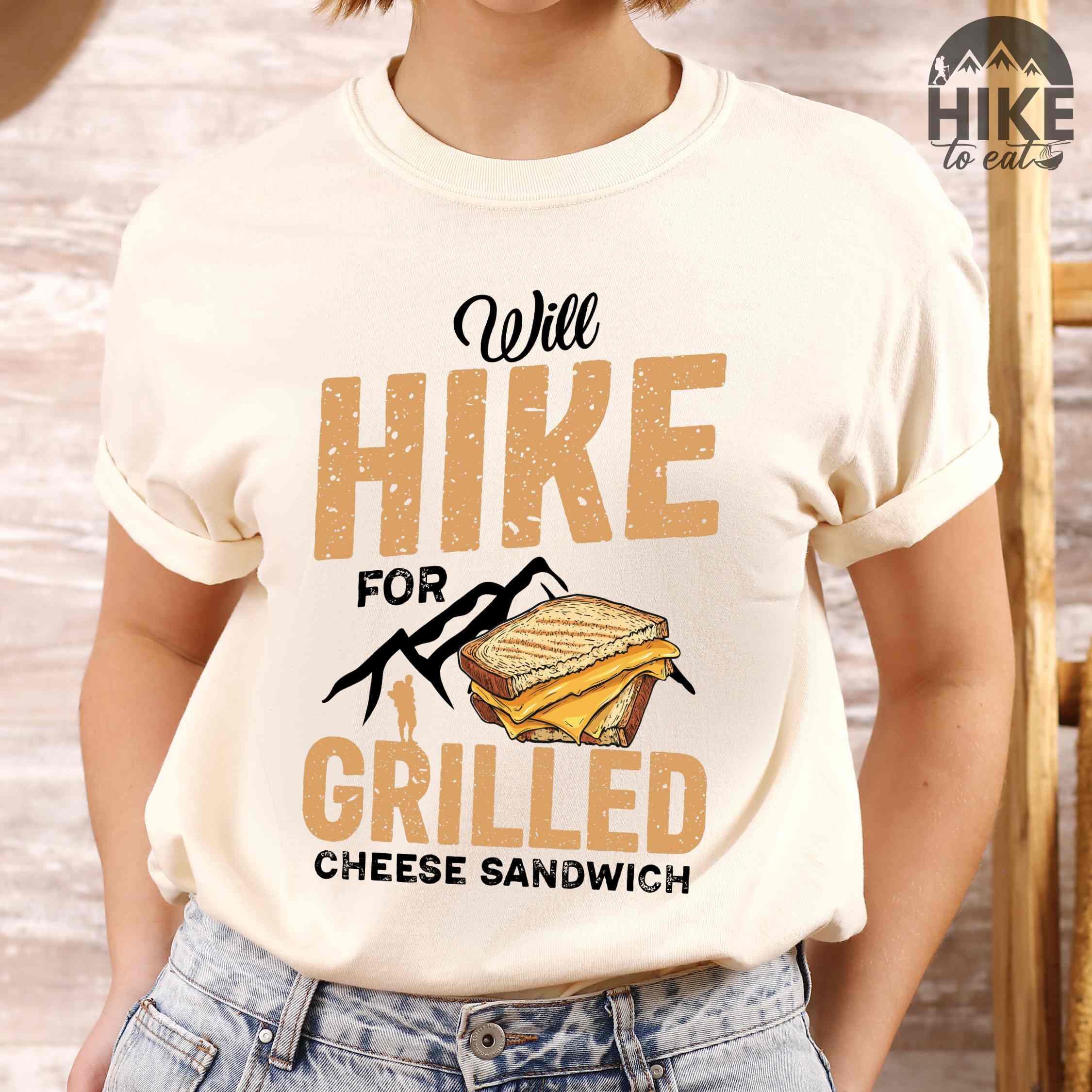 woman wearing ivory "will hike for grilled cheese sandwich" colored vintage tee with bold typography, mountains, birds, illustrated grilled cheese sandwich, and backpackers for sandwich enthusiasts