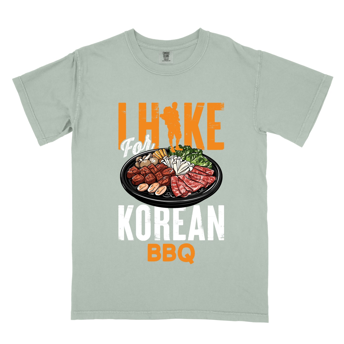 Bay (Light Gray) t-shirt with orange and white text reading "I HIKE For KOREAN BBQ". "I HIKE" appears in large distressed orange letters at the top with a hiker silhouette integrated into the letter "I", "For" in white script in the middle, "KOREAN" in large distressed white letters, and "BBQ" in orange at the bottom. Features a detailed illustration of Korean barbecue with meat, mushrooms, and vegetables on a black plate in between "For" and "KOREAN."