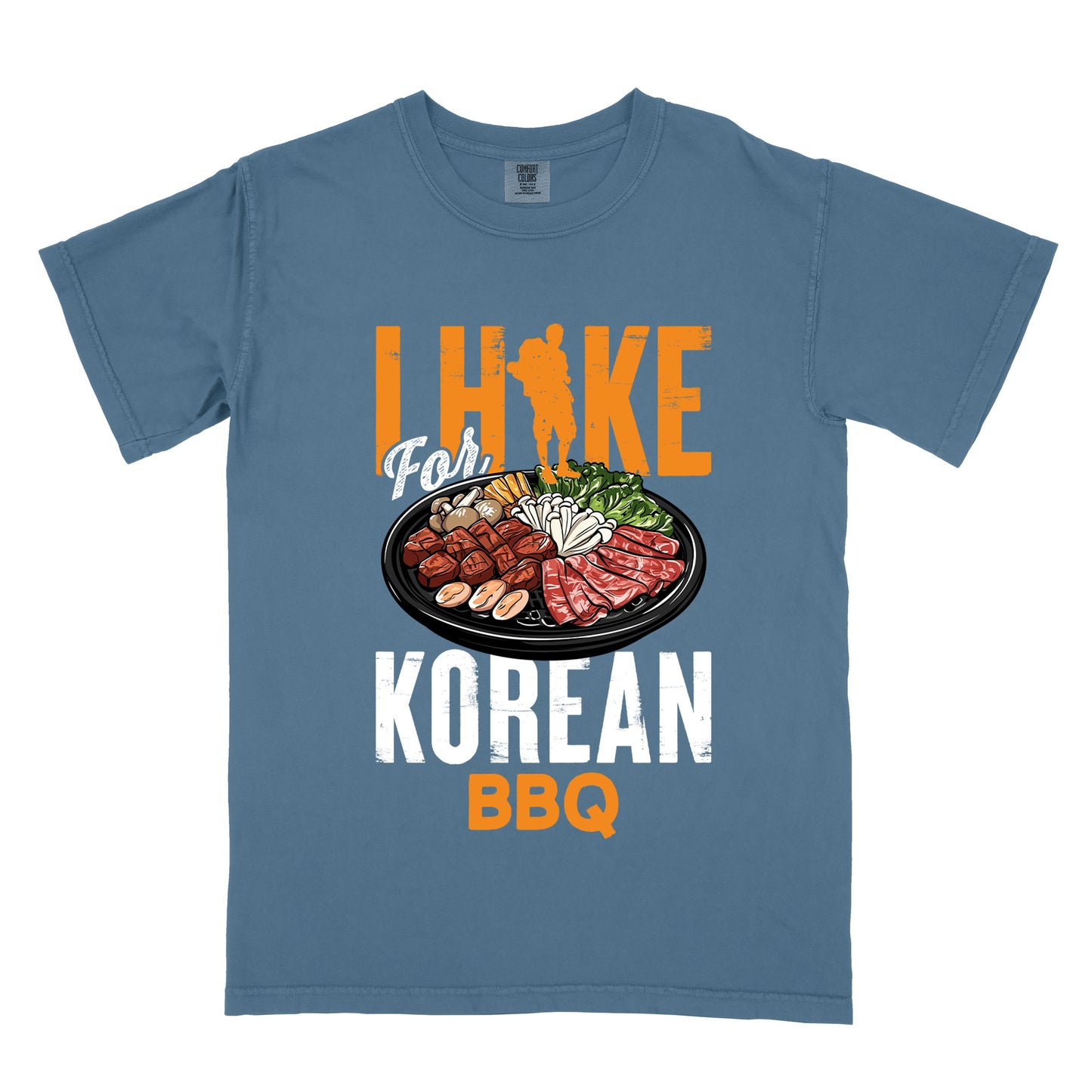 Blue Jean (Denim Blue) t-shirt with orange and white text reading "I HIKE For KOREAN BBQ". "I HIKE" appears in large distressed orange letters at the top with a hiker silhouette integrated into the letter "I", "For" in white script in the middle, "KOREAN" in large distressed white letters, and "BBQ" in orange at the bottom. Features a detailed illustration of Korean barbecue with meat, mushrooms, and vegetables on a black plate in between "For" and "KOREAN."