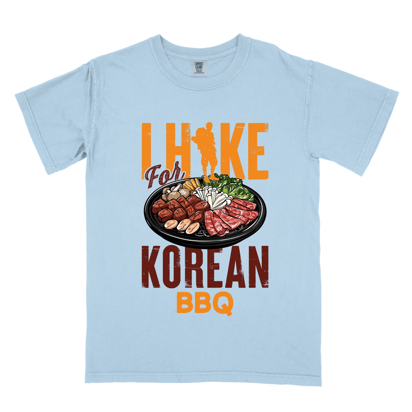 Chambray (Light Blue) t-shirt with orange and red text reading "I HIKE For KOREAN BBQ". "I HIKE" appears in large distressed orange letters at the top with a hiker silhouette integrated into the letter "I", "For" in red script in the middle, "KOREAN" in large distressed red letters, and "BBQ" in orange at the bottom. Features a detailed illustration of Korean barbecue with meat, mushrooms, and vegetables on a black plate in between "For" and "KOREAN."