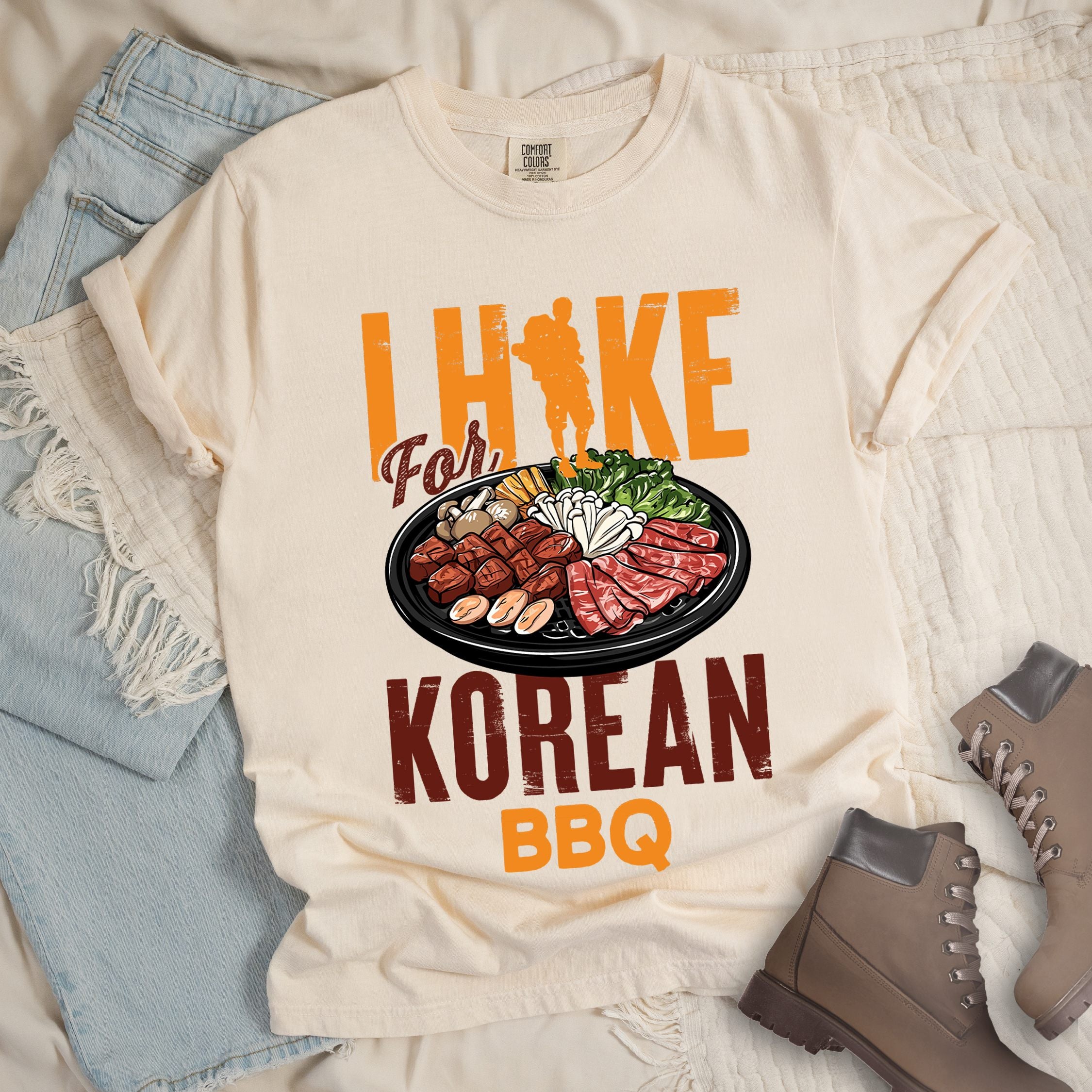 Ivory shirt with Hiking Design featuring the phrase “I Hike for Korean BBQ” with a hiker silhouette and a platter of Korean barbecue with side dishes.