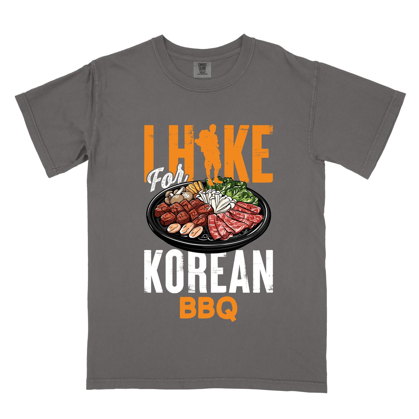 Pepper (Dark Gray) t-shirt with orange and white text reading "I HIKE For KOREAN BBQ". "I HIKE" appears in large distressed orange letters at the top with a hiker silhouette integrated into the letter "I", "For" in white script in the middle, "KOREAN" in large distressed white letters, and "BBQ" in orange at the bottom. Features a detailed illustration of Korean barbecue with meat, mushrooms, and vegetables on a black plate in between "For" and "KOREAN."