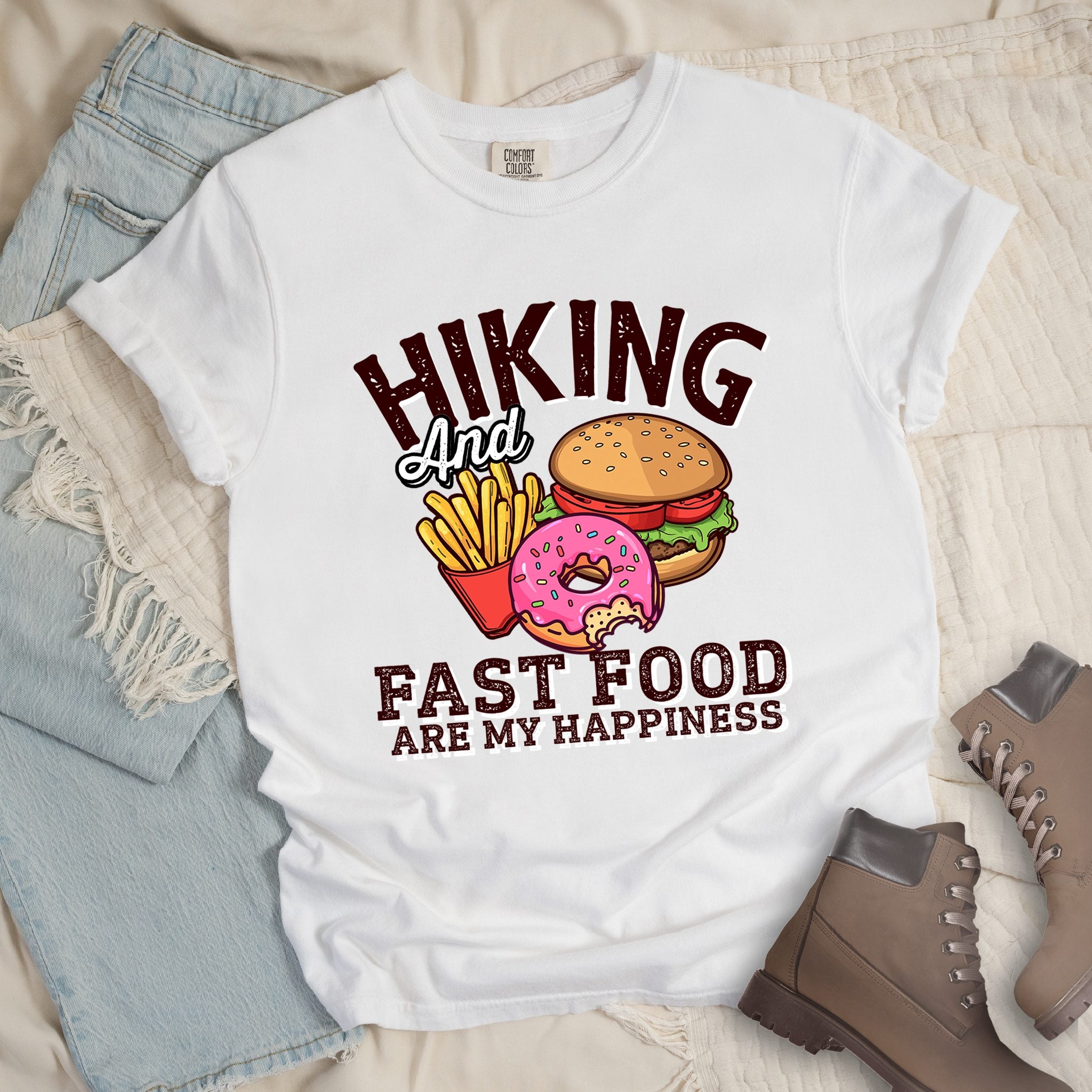 White shirt showing a hiking design with 'Hiking and fast food are my happiness' phrase and an illustration of fast food meal in front.