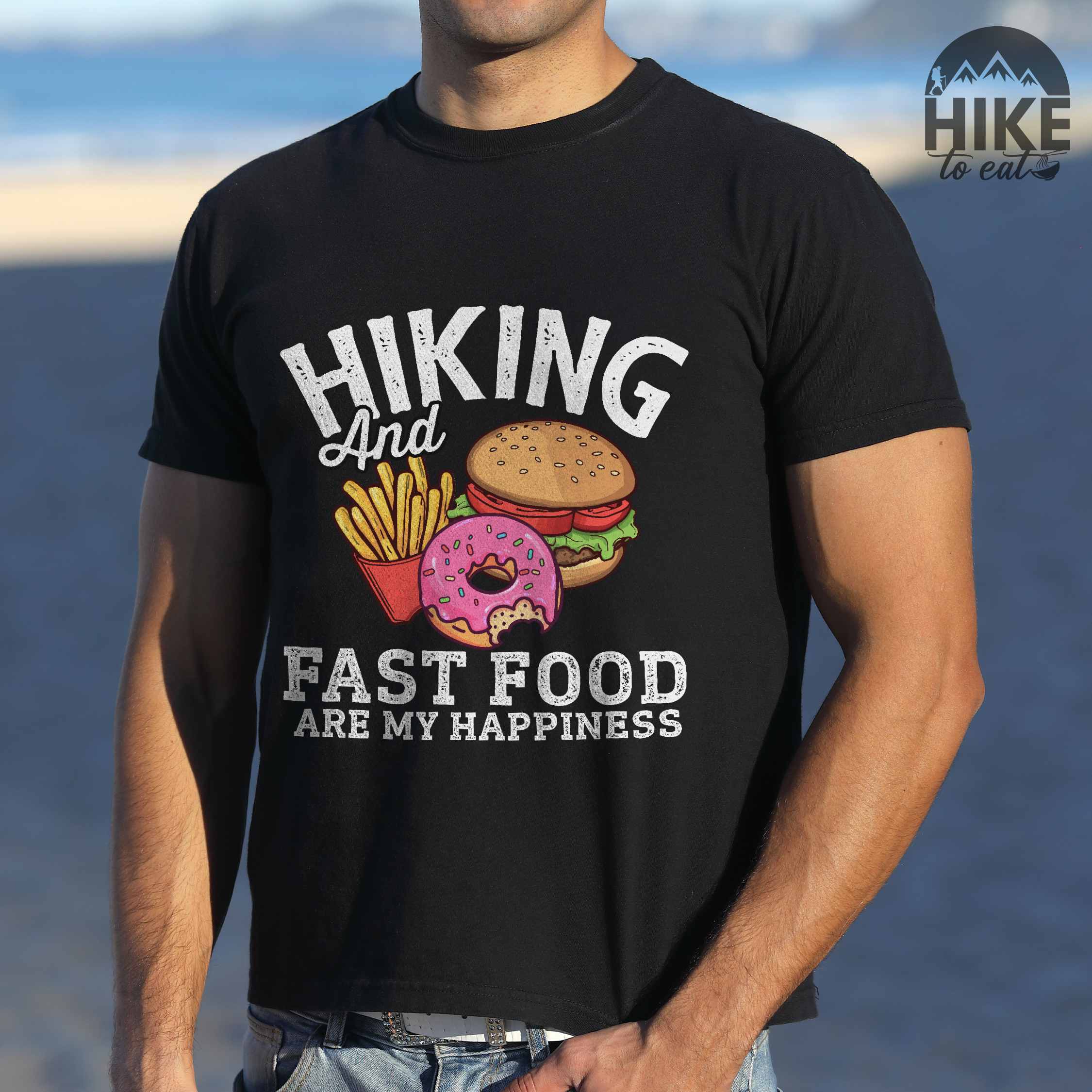 Man wearing black "Hiking and Fast Food are my Happiness" colored vintage tee with bold typography, and illustrated fast food meal for the hikers who wants a rewarding meal.