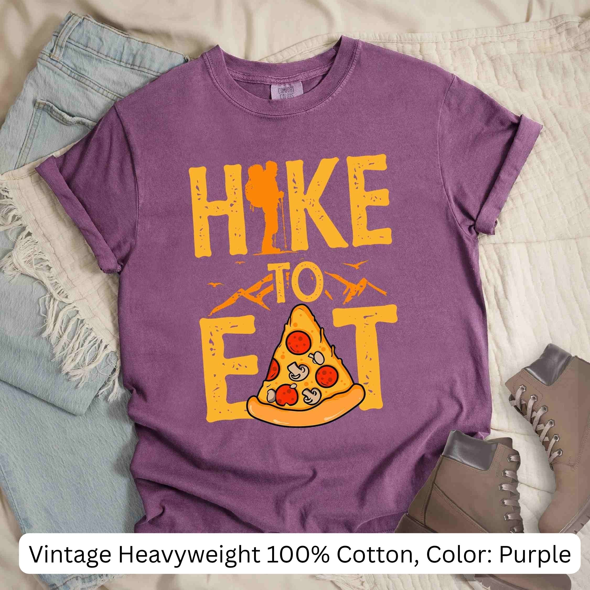 Purple t-shirt with 'Hike to Eat' and pizza graphic on a textured surface. Vintage Heavyweight 100% Cotton color: purple