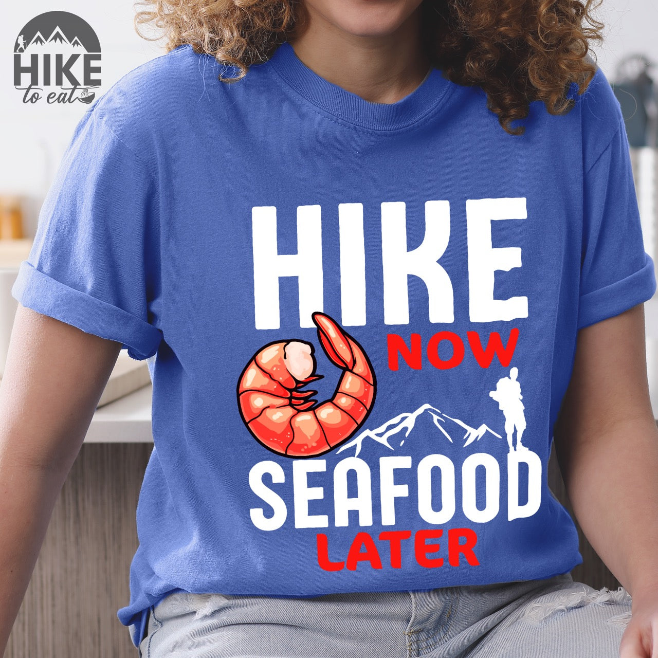 Woman wearing funny hiking motivation shirt for seafood lovers featuring bold NOW LATER typography, realistic shrimp graphic, mountain landscape illustration, and hiker silhouette on premium outdoor adventure tee perfect gift for trail enthusiasts who love fresh ocean food in flo blue color 
