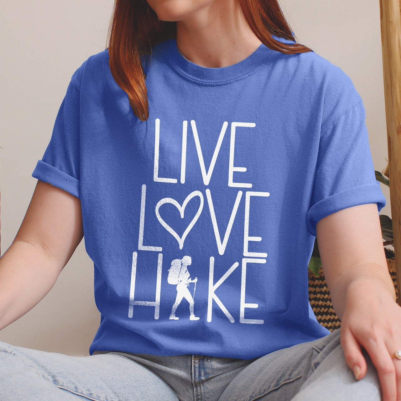 Woman wearing flo blue (bluish violet) Women's hiking lifestyle shirt Live Love Hike with minimalist stacked typography heart symbol and female hiker silhouette on Comfort Colors tee for outdoor enthusiasts celebrating trail passion and for hikers and foodies