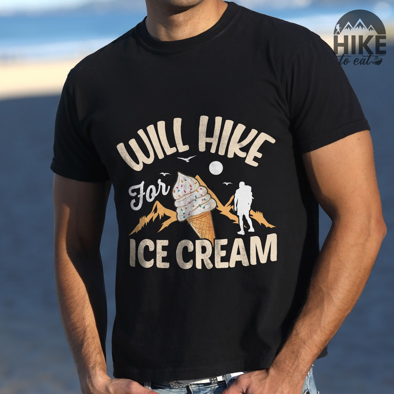Man wearing black Will Hike for Ice Cream statement tee with curved typography, script lettering, mountain peaks, hiker silhouette, and ice cream cone illustration on Comfort Colors shirt for dessert-loving outdoor enthusiasts
