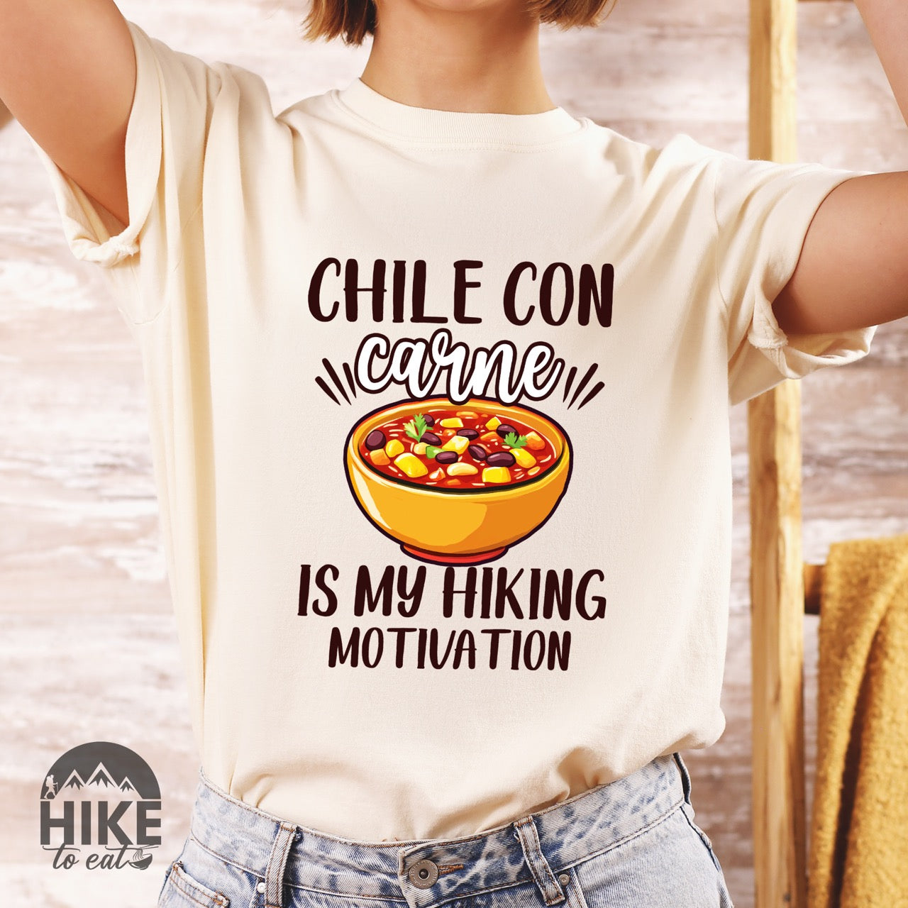 Woman wearing ivory Chile con carne is my Hiking Motivation statement tee with bold typography, script lettering, and colorful chili bowl illustration for comfort food-loving outdoor enthusiasts