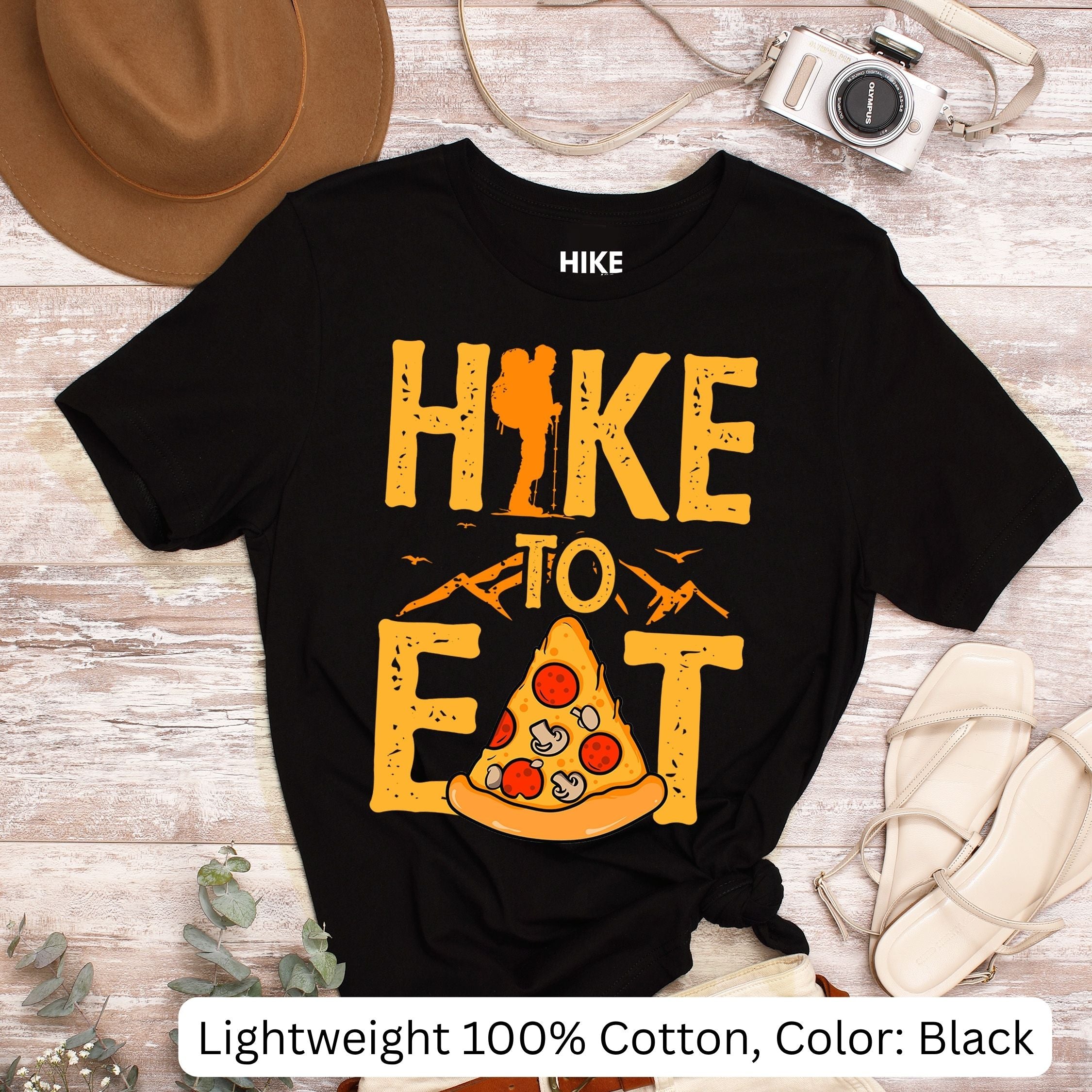 Black t-shirt with 'Hike to Eat' pizza graphic on a wooden surface with accessories. Lightweight 100% Cotton, color: black