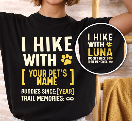 Black graphic t-shirt with 'Trail Buddies Personalized' design featuring 'I Hike with' text and customizable pet name field in cream and yellow lettering with paw prints, plus customizable year for 'buddies since' and trail memories infinity, shown with close-up detail.