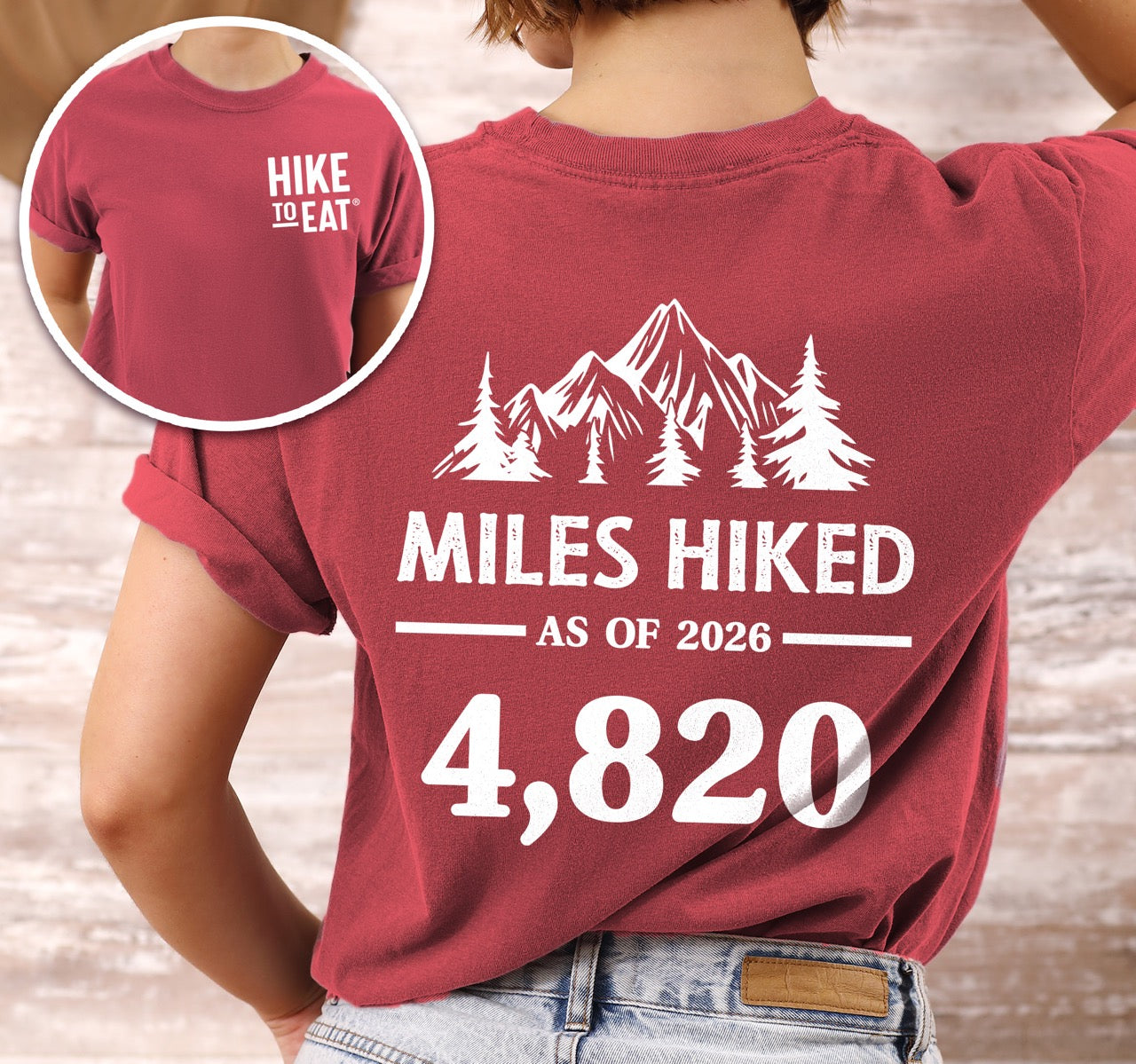Woman wearing crimson (red)  t-shirt with Hike to Eat logo on front chest, back featuring MILES HIKED AS OF 2026 text with personalized number field, mountain and pine tree silhouettes, customizable achievement tracker design - perfect for hikers. 