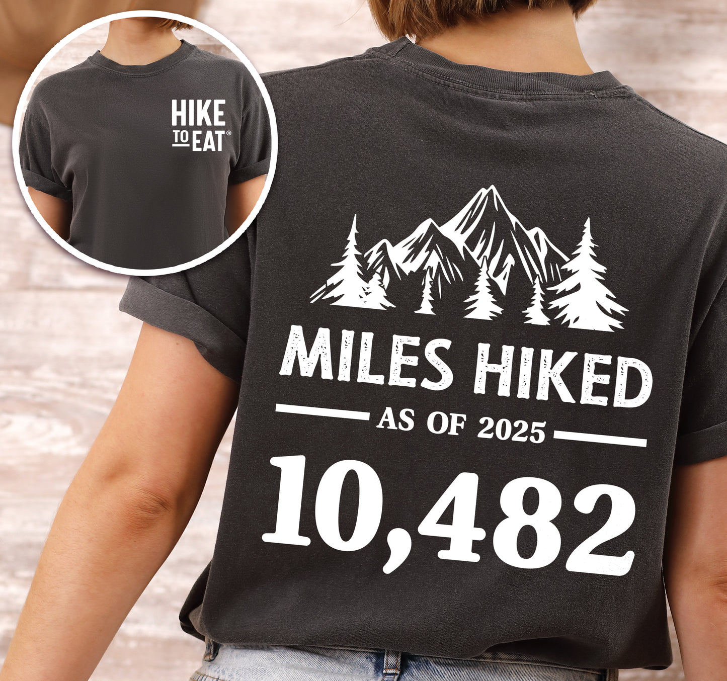 Pepper (Dark Gray) Hike to Eat t-shirt front and back view showing small white chest detail and large back design featuring 'Milestone Tracker Personalized' with mountain and pine tree silhouettes, 'Miles Hiked as of 2025' text and customizable numbers field, displaying example number 10,482.