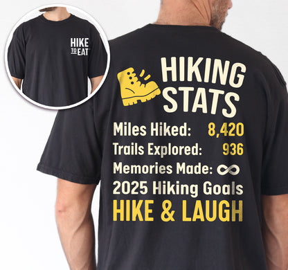 Black Hike to Eat t-shirt front and back view showing small chest detail and large back design featuring 'Hiking Stats Personalized' with yellow hiking boot icon, customizable miles hiked and trails explored numbers, memories made infinity, and customizable 2025 hiking goals, displaying example stats and 'Hike & Laugh' goal.