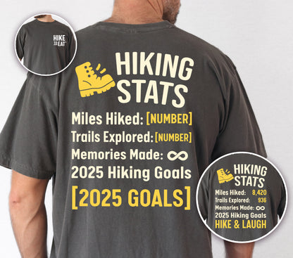 Pepper (Dark Gray) Hike to Eat t-shirt front and back view showing small white chest detail and large back design featuring 'Hiking Stats Personalized' with yellow hiking boot icon, customizable miles hiked and trails explored numbers, memories made infinity, and customizable 2025 hiking goals, shown with close-up detail displaying example stats and 'Hike & Laugh' goal.