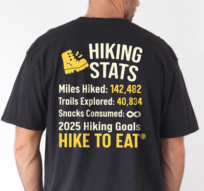 Black Hike to Eat t-shirt front and back view showing small chest detail and large back design featuring 'Hiking Stats' design with yellow hiking boot icon, customizable miles hiked and trails explored numbers, snacks consumed infinity, and 2025 hiking goals 'Hike to Eat ®'. 