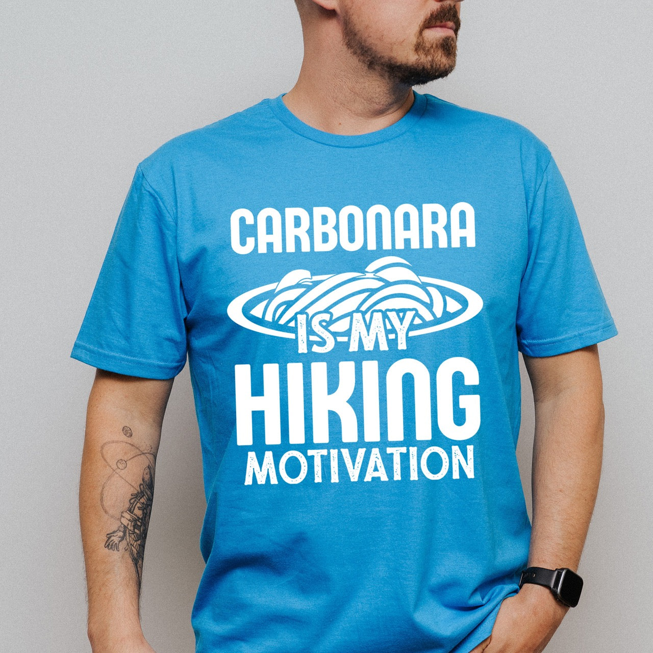 Man wearing saphire (blue) Carbonara is my Hiking Motivation statement tee with bold typography and pasta bowl illustration for carbonara enthusiasts and hikers