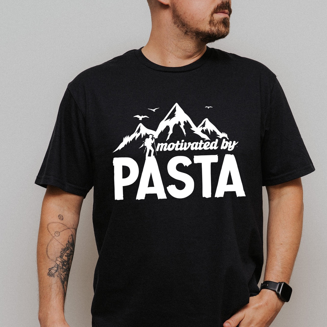 man wearing black motivated by Pasta statement tee with mountains, birds, and hiker silhouette for pasta enthusiasts and hikers