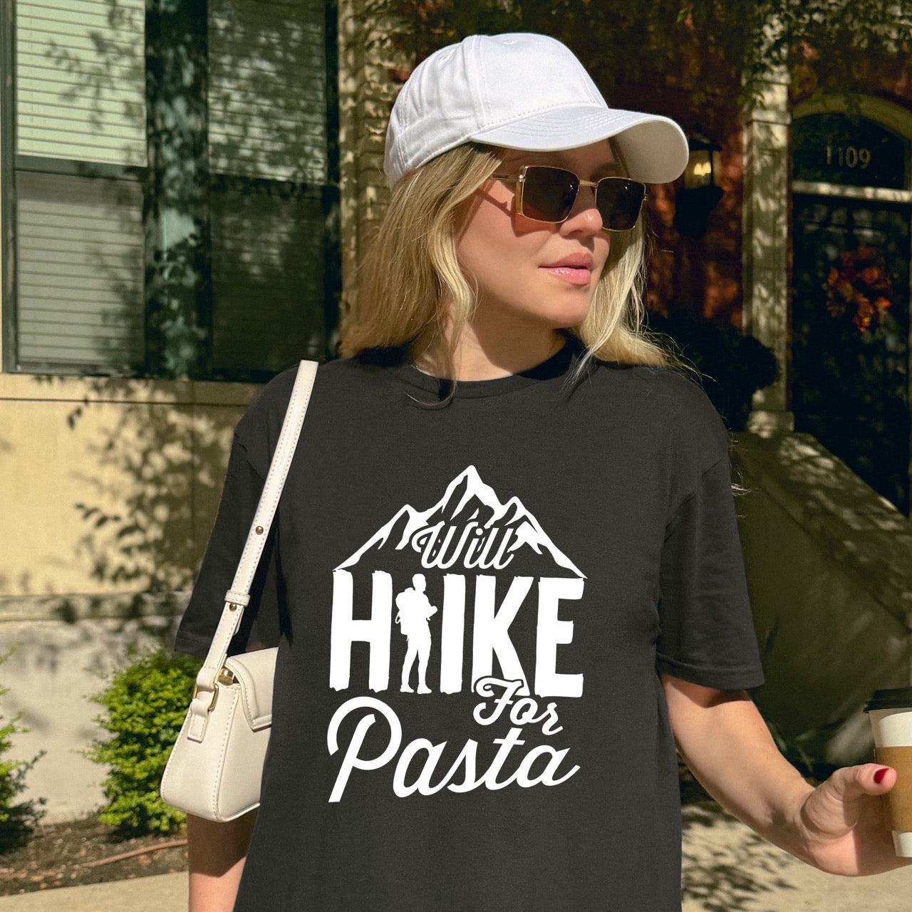 woman wearing black Will Hike for Pasta statement tee with bold typography, mountain peaks, and backpacker silhouette for pasta devotees and hikers
