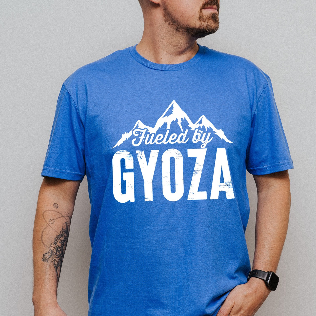 man wearing royal (blue) Fueled by Gyoza statement tee with distressed bold typography and mountain peaks for dumpling enthusiasts and hikers