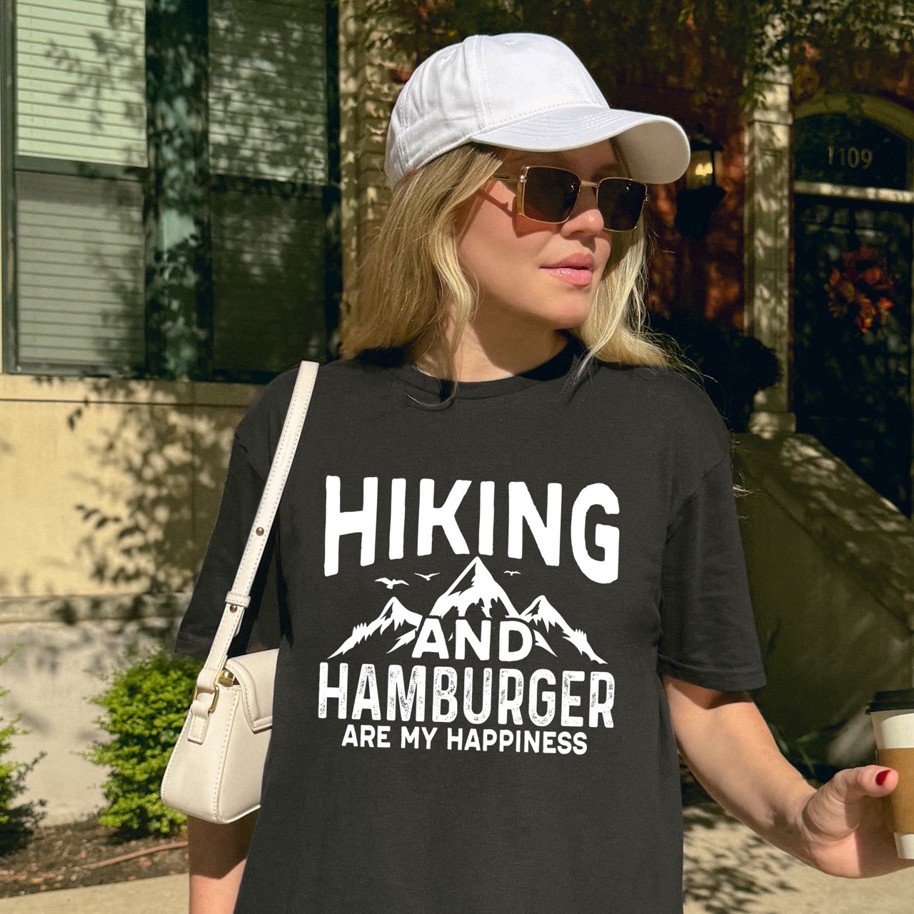 woman wearing black  Hiking and Hamburger are my Happiness statement tee with distressed bold typography, mountain peaks, flying birds, and pine trees for burger-loving outdoor enthusiasts and hikers