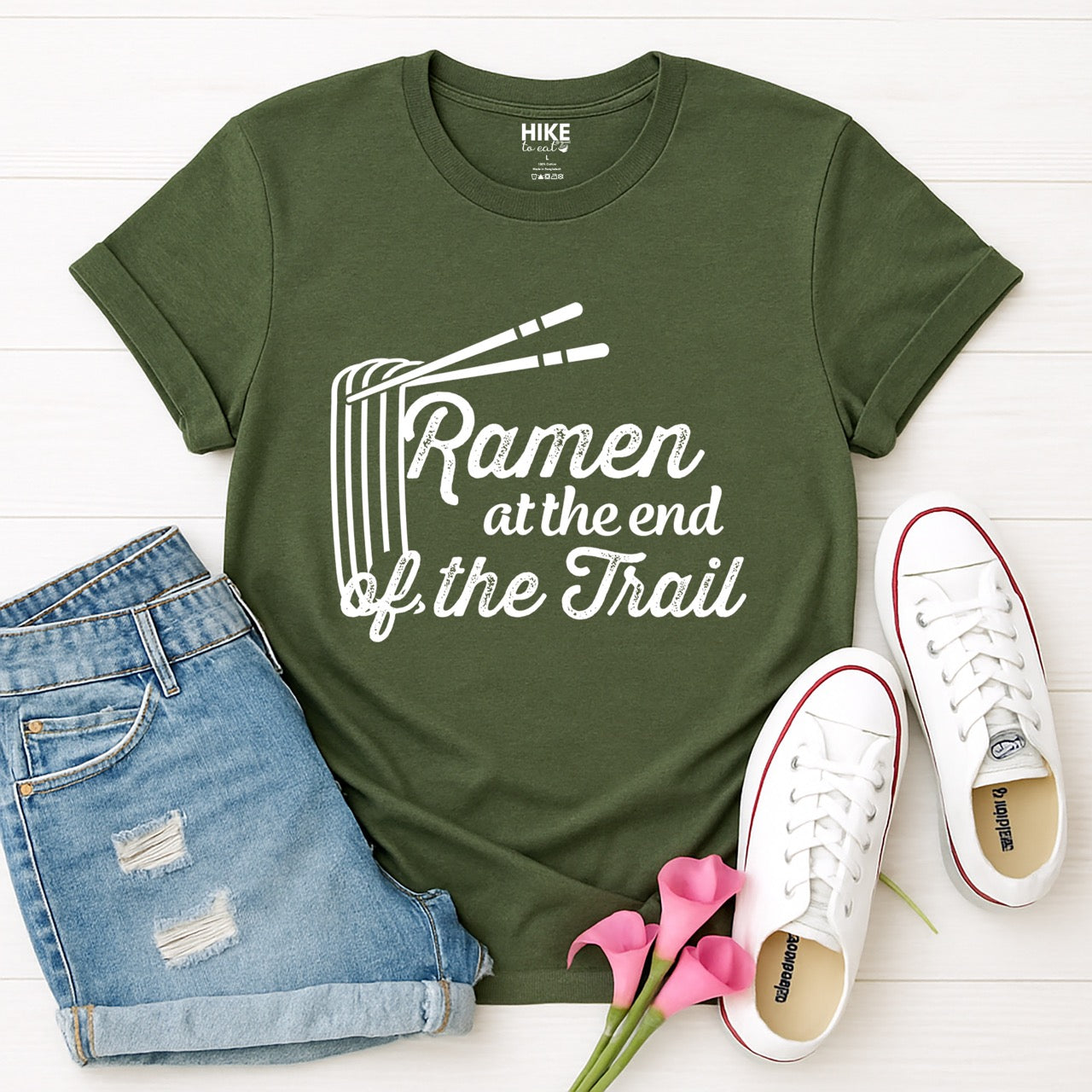 Military Green Ramen at the End of the Trail statement tee with elegant script typography, ramen bowl illustration, and chopsticks for Japanese noodle-loving outdoor enthusiasts, foodies and hikers  layed flat with shoes and jeans. 